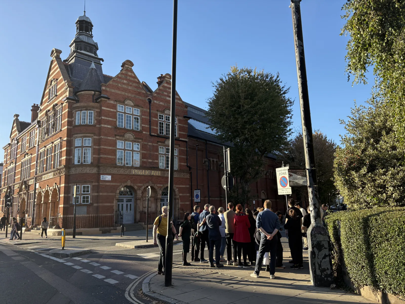 people staning on a street corner looking at a large red brick building