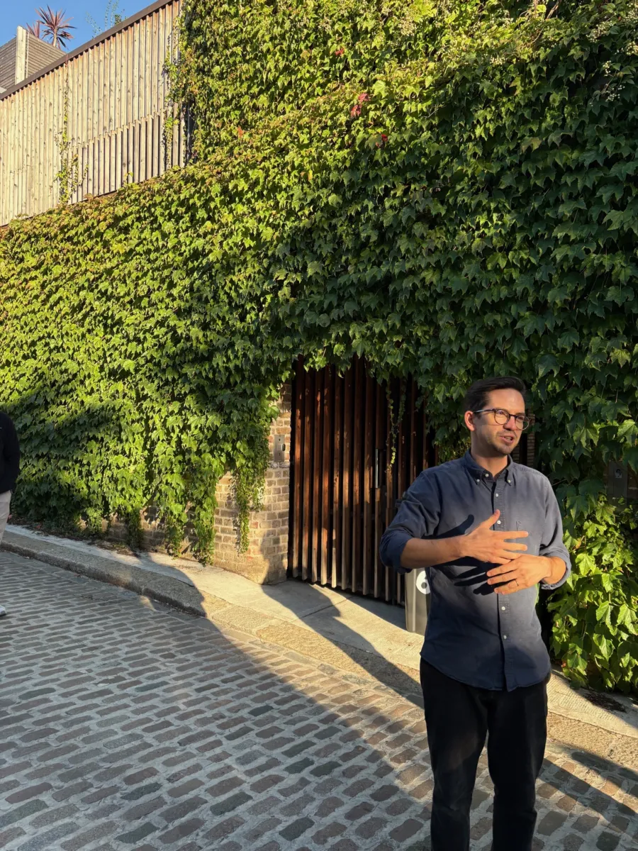 A man stabing in front of a brick home which is covered on greenery