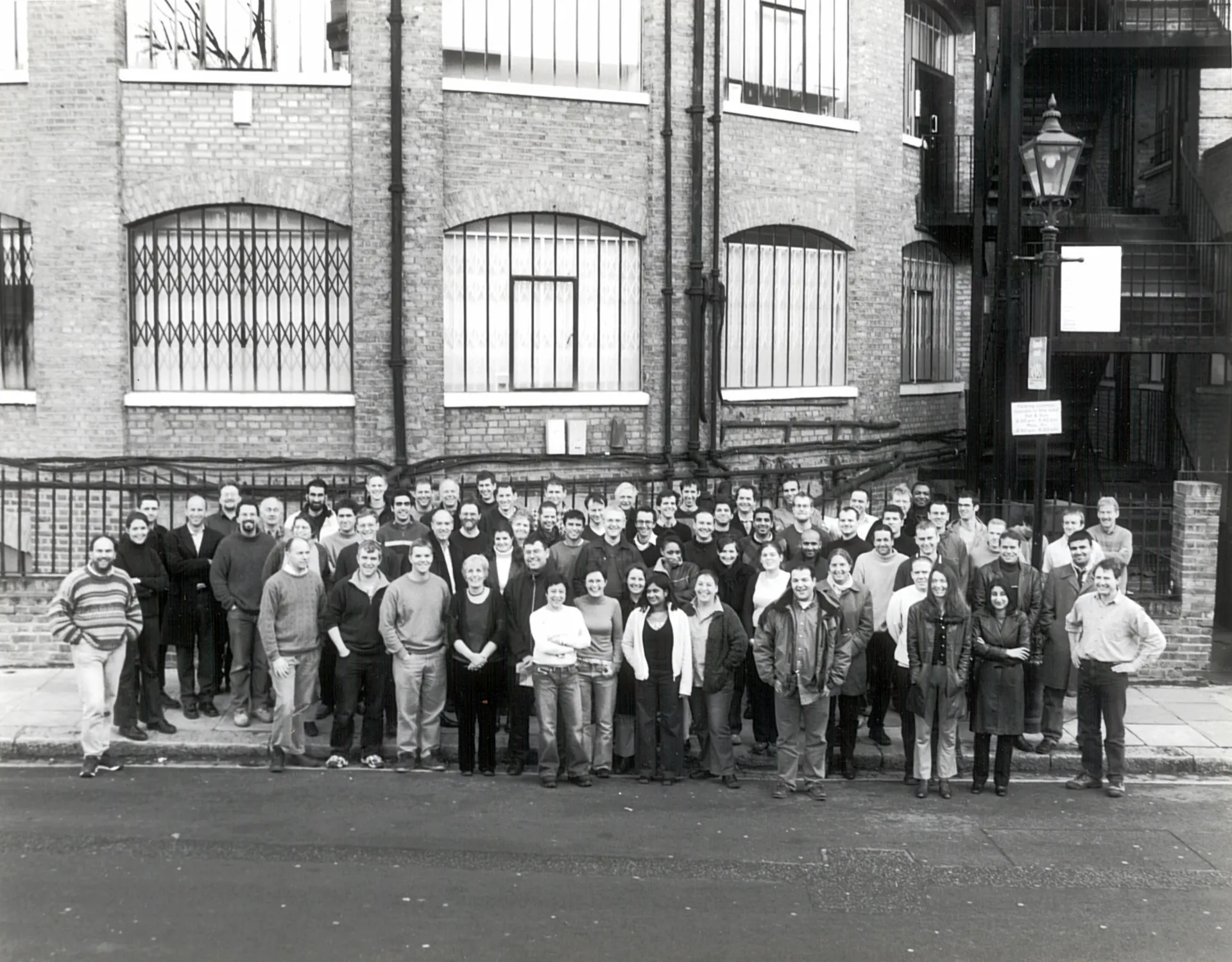 A black and white photo with a group of more than 20 people standing in front of the Max Fordham London office, the Rotunda.