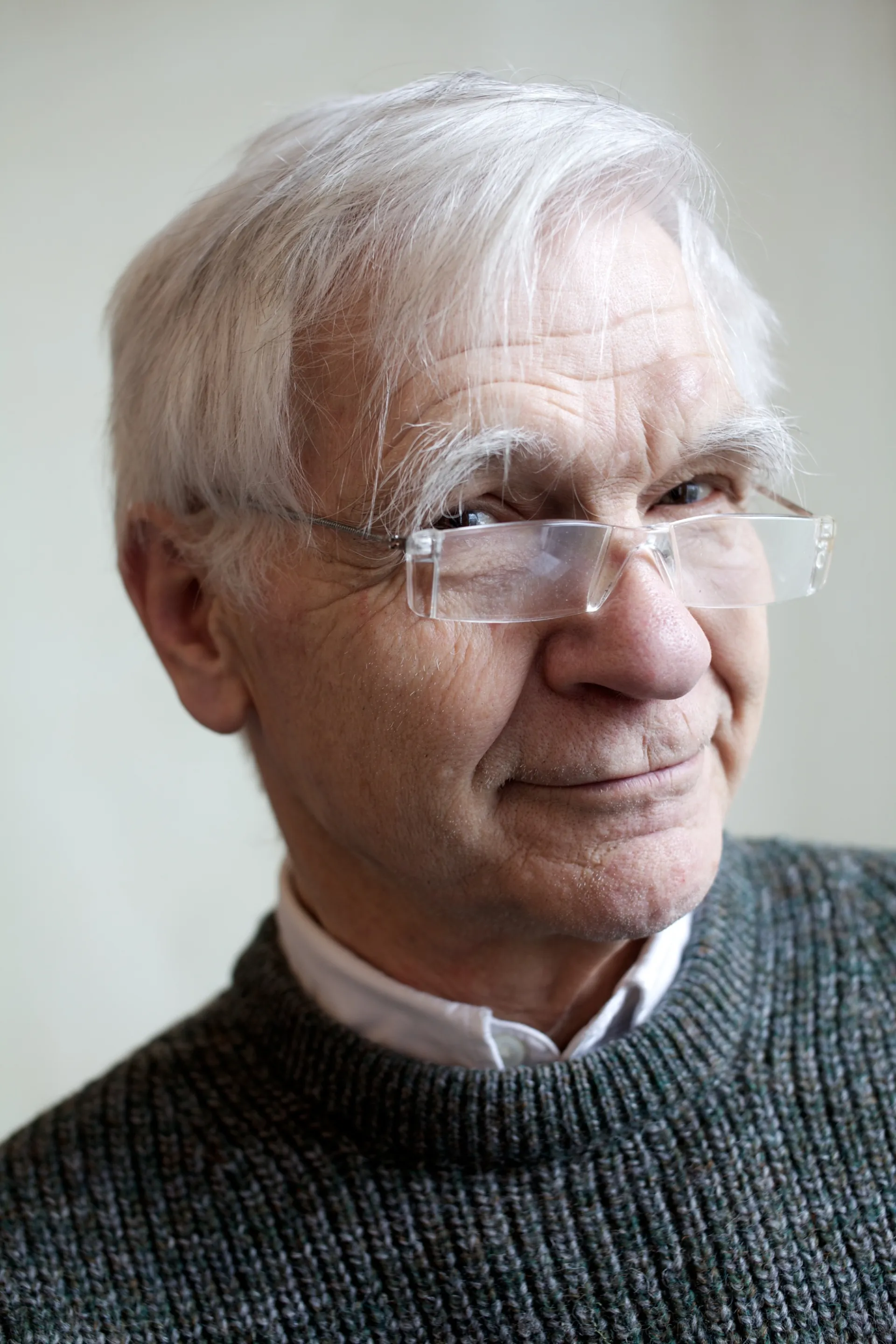 Close-up portrait shot of Max Fordham as an elderly man, looking over the top of his reading glasses and slightly smiling at the viewer.