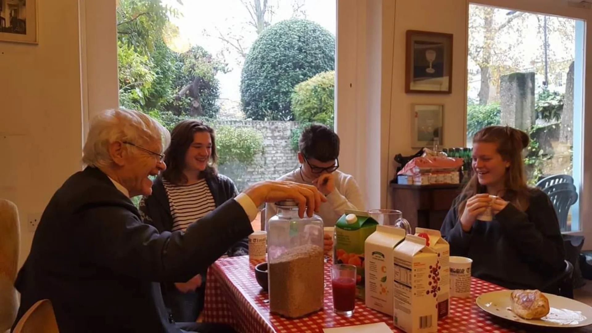 Max in his 80s, sat around a table at home with his grandchildren, all laughing together.
