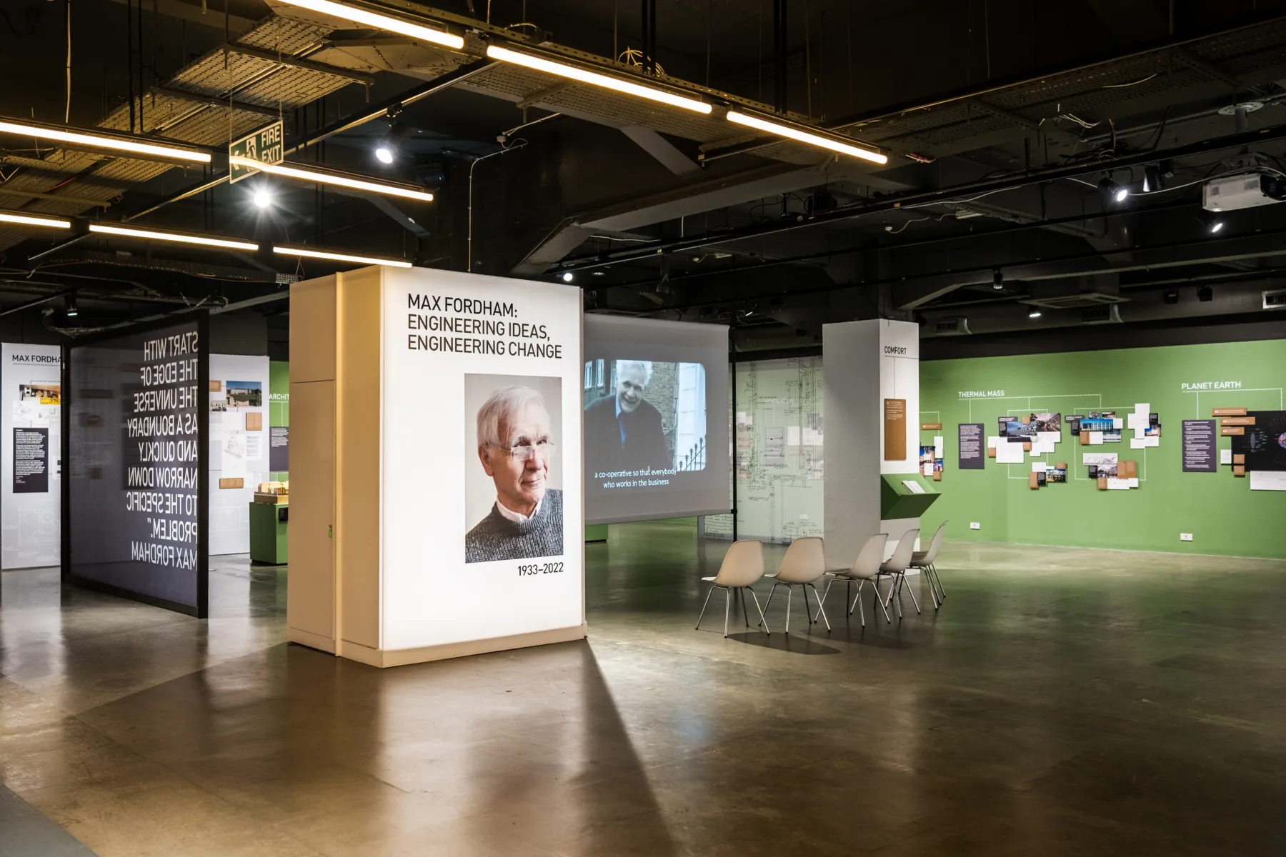 A landscape photo showing an indoor exhibition venue, a lightbox with Max Fordham's photo on and it writes 'Engineering Ideas, Engineering Change'