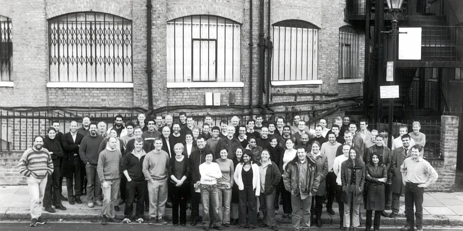 A black and white photo with a group of more than 20 people standing in front of the Max Fordham London office, the Rotunda.