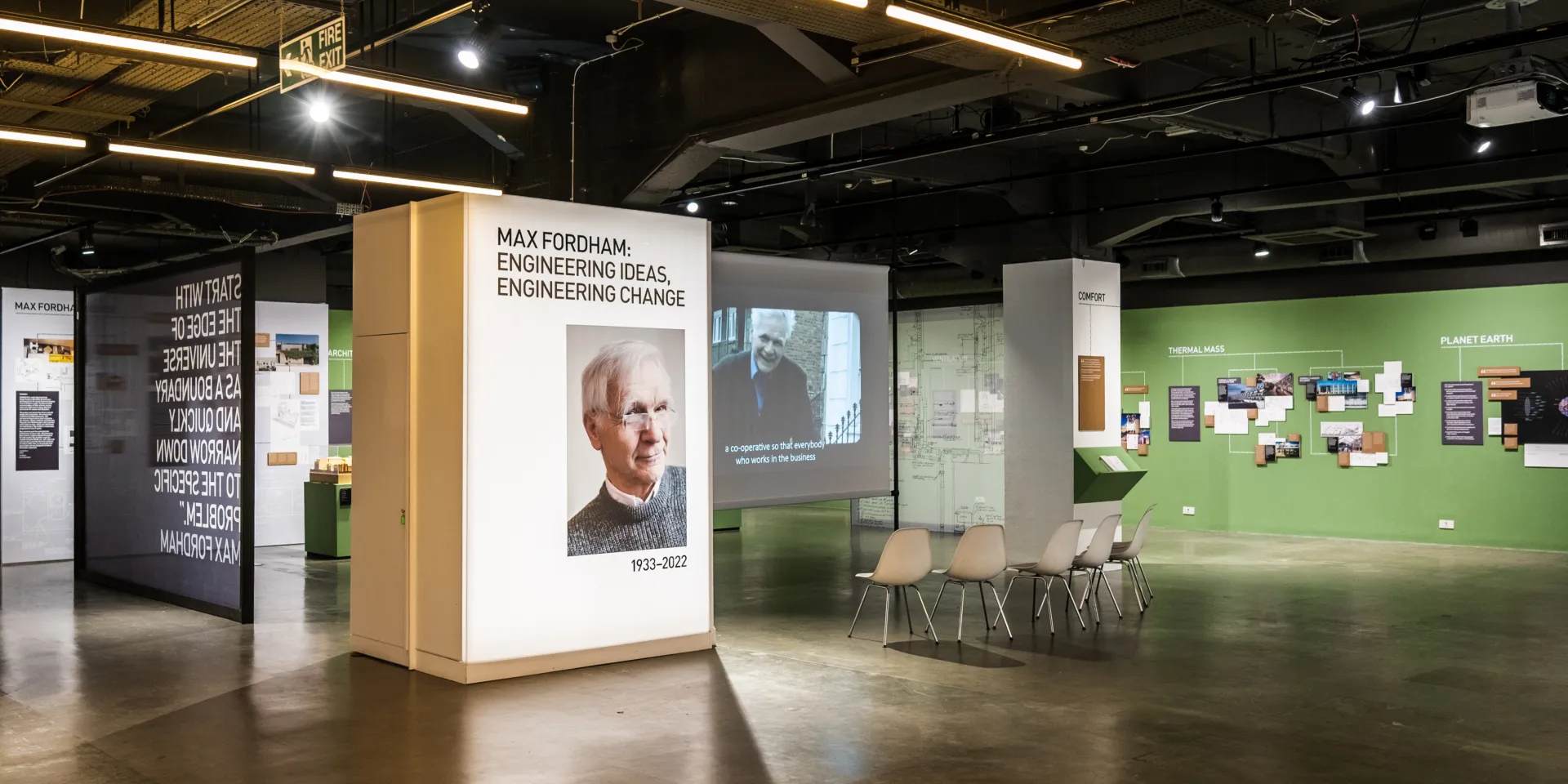 A landscape photo showing an indoor exhibition venue, a lightbox with Max Fordham's photo on and it writes 'Engineering Ideas, Engineering Change'