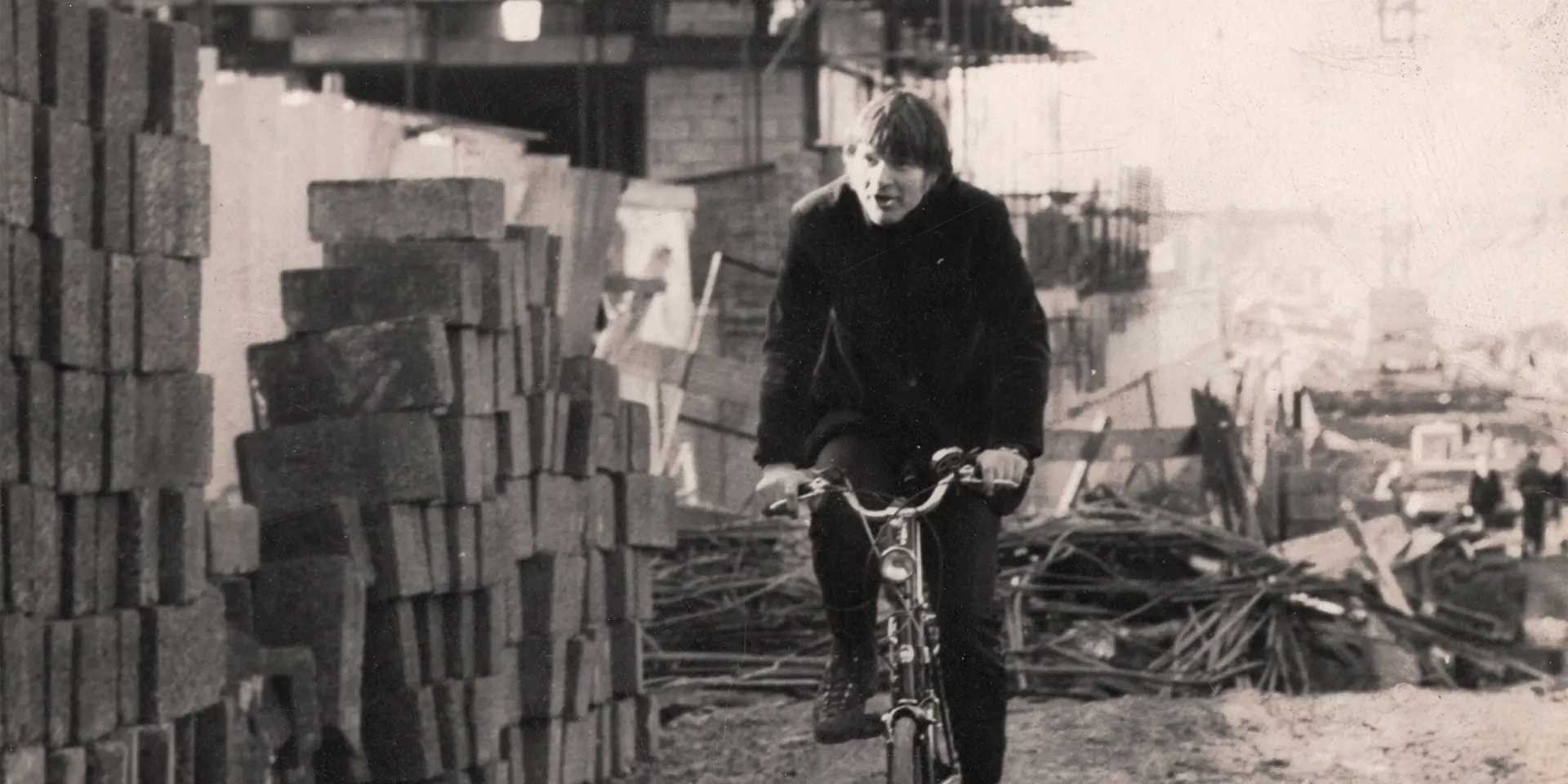 1960s black and white photo of Max cycling past a building site.