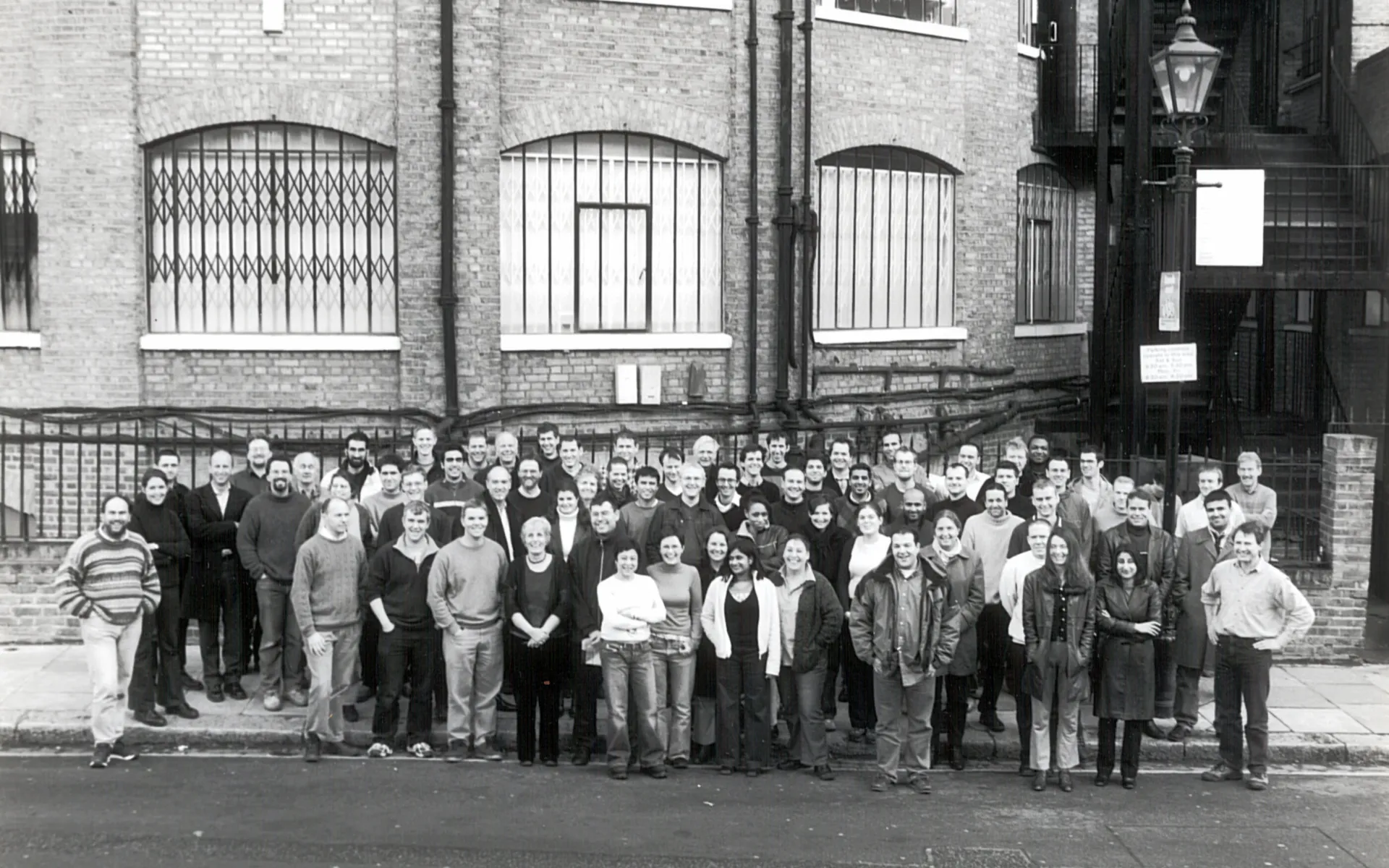 A black and white photo with a group of more than 20 people standing in front of the Max Fordham London office, the Rotunda.