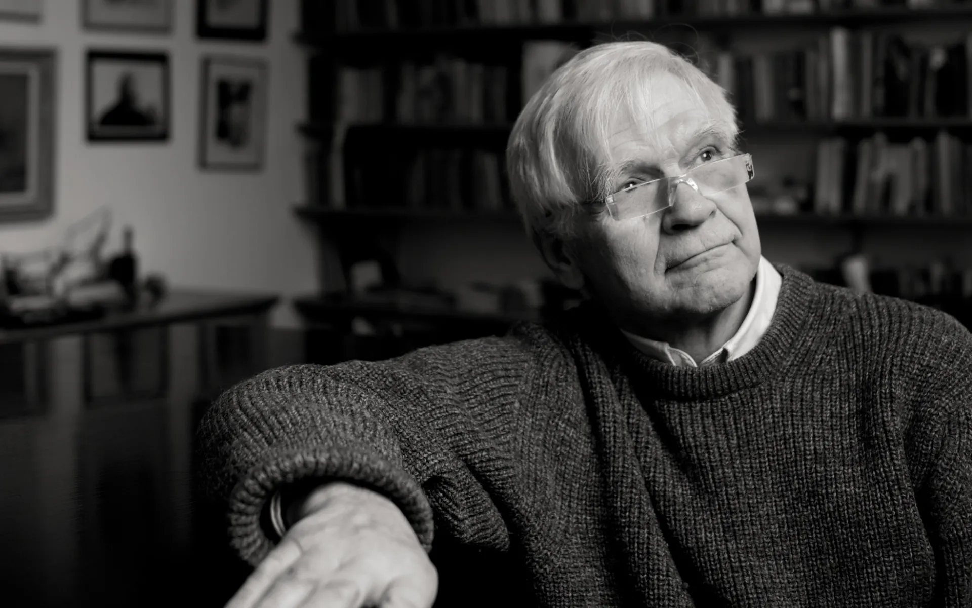 Black and white close-up photo of Max sat down at home, wearing a jumper and shirt, looking away from the viewer.