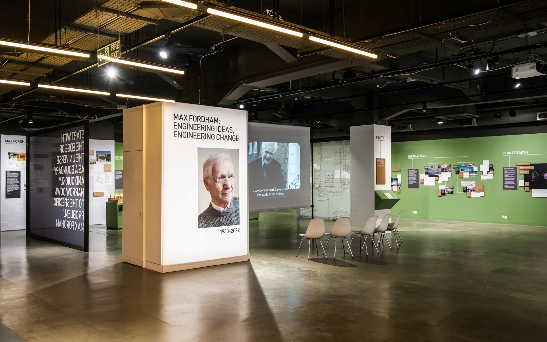 A landscape photo showing an indoor exhibition venue, a lightbox with Max Fordham's photo on and it writes 'Engineering Ideas, Engineering Change'