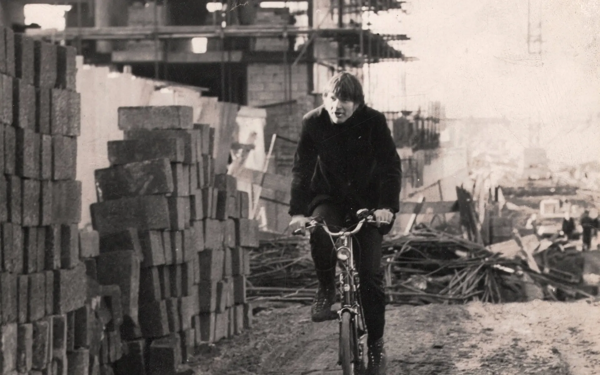 1960s black and white photo of Max cycling past a building site.