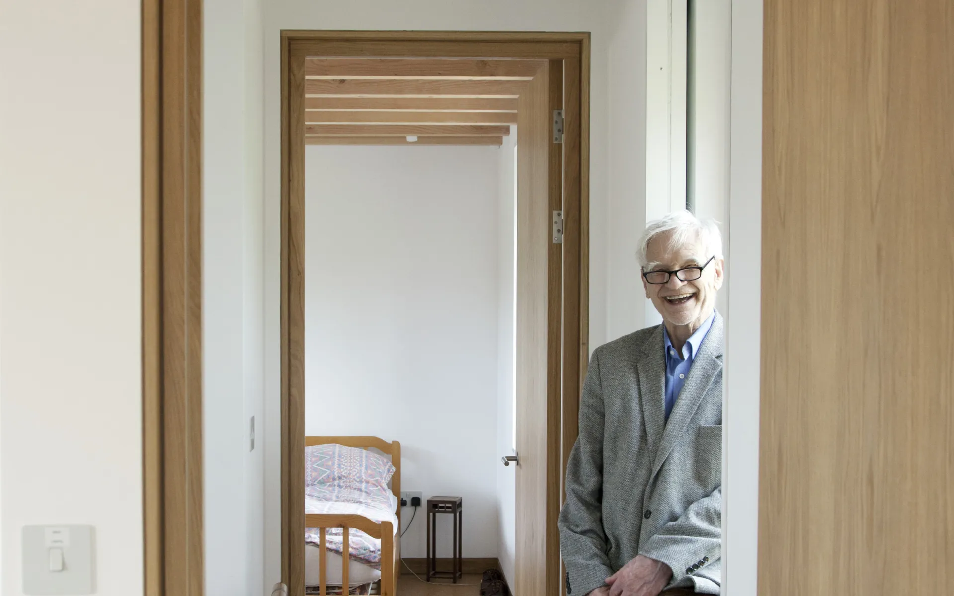 Colour photo of Max as an elderly man, smiling at the camera and leaning on a windsill in the upstairs of his new house in Camden.