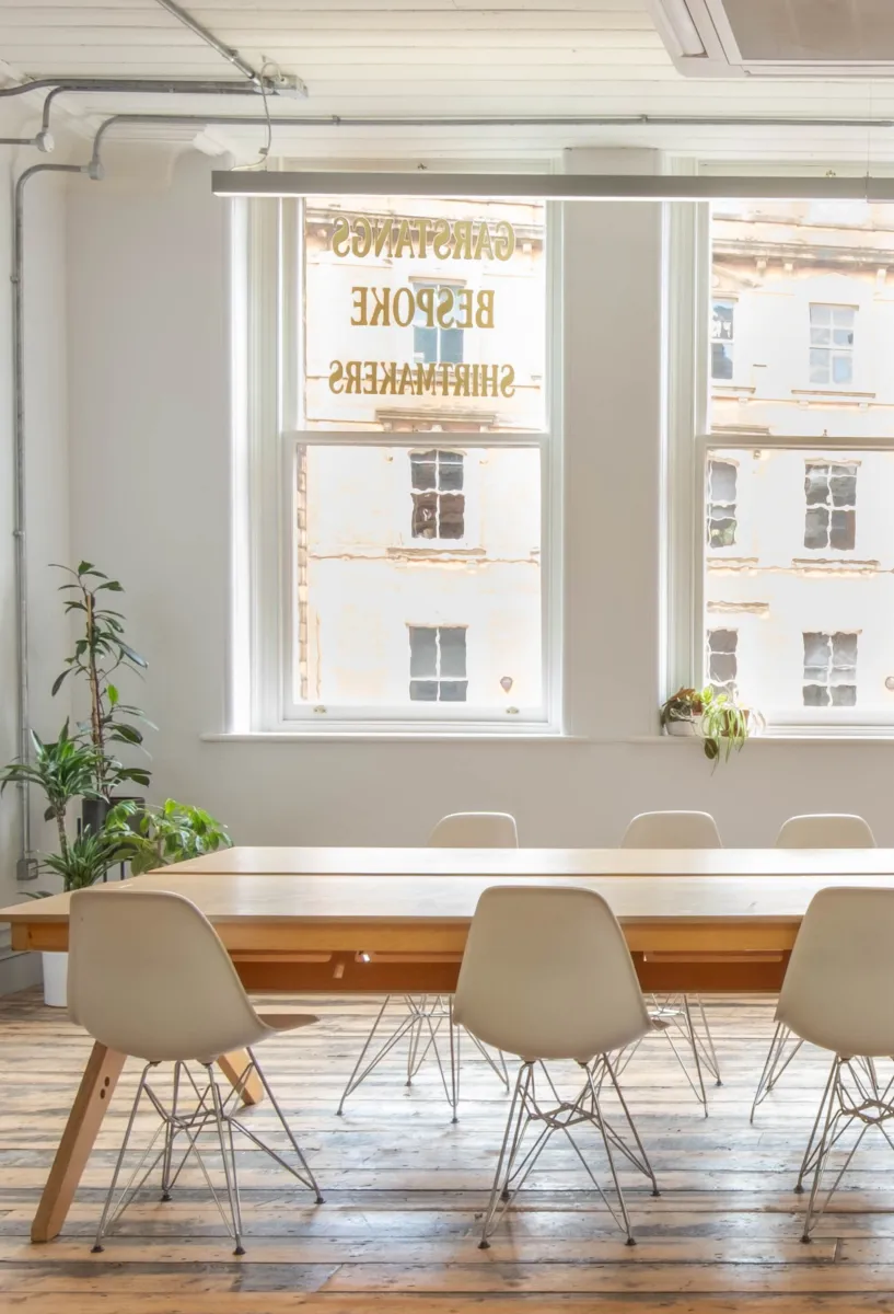 Interior photo of large meeting table and chairs in an open plan office with four windows and lots of daylight.