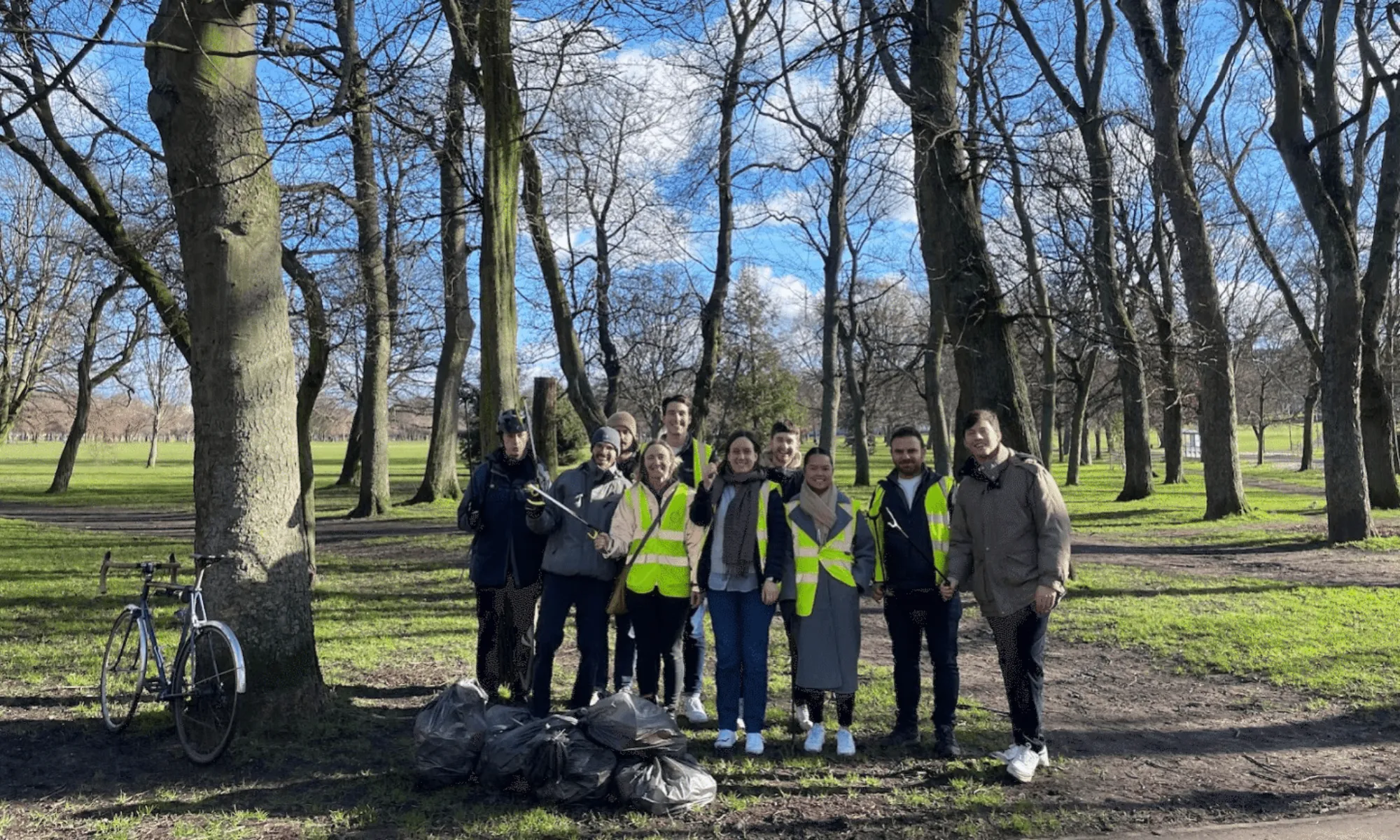 Ten people wearing high visibility vests with litter pickers on their hands in a park
