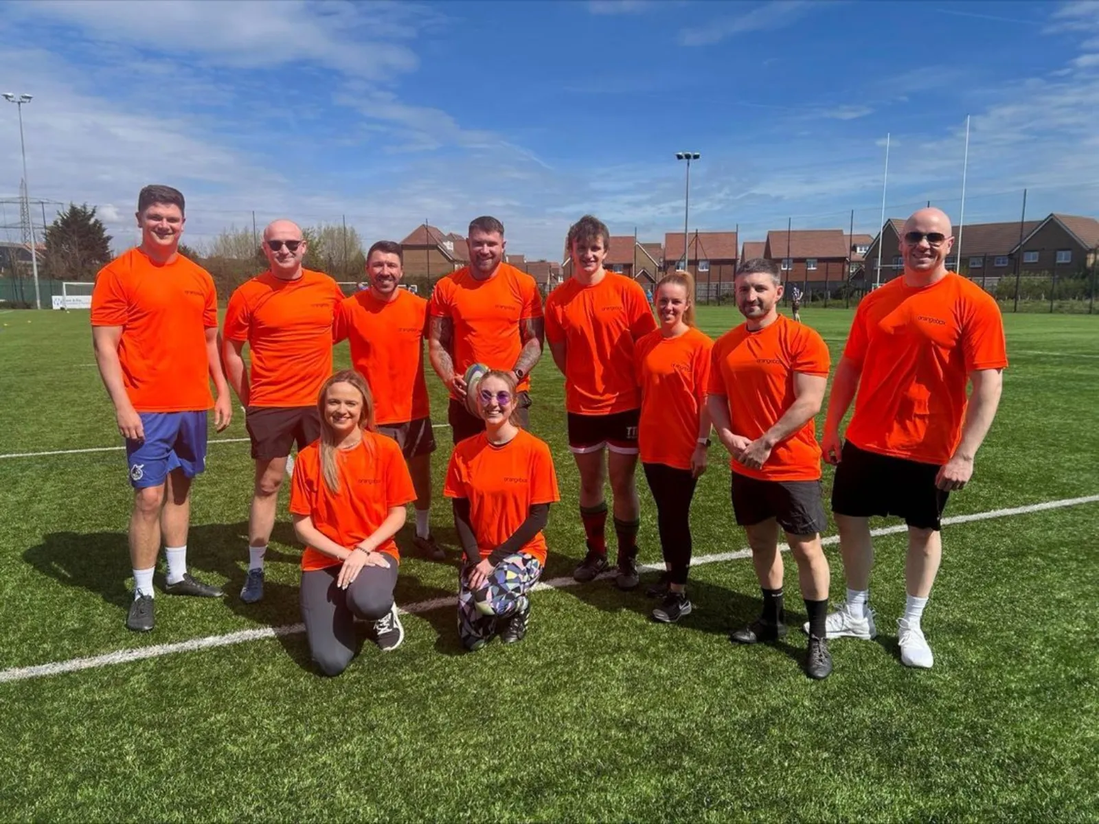 Ten people wearing team orange t-shirts smiling in a pitch