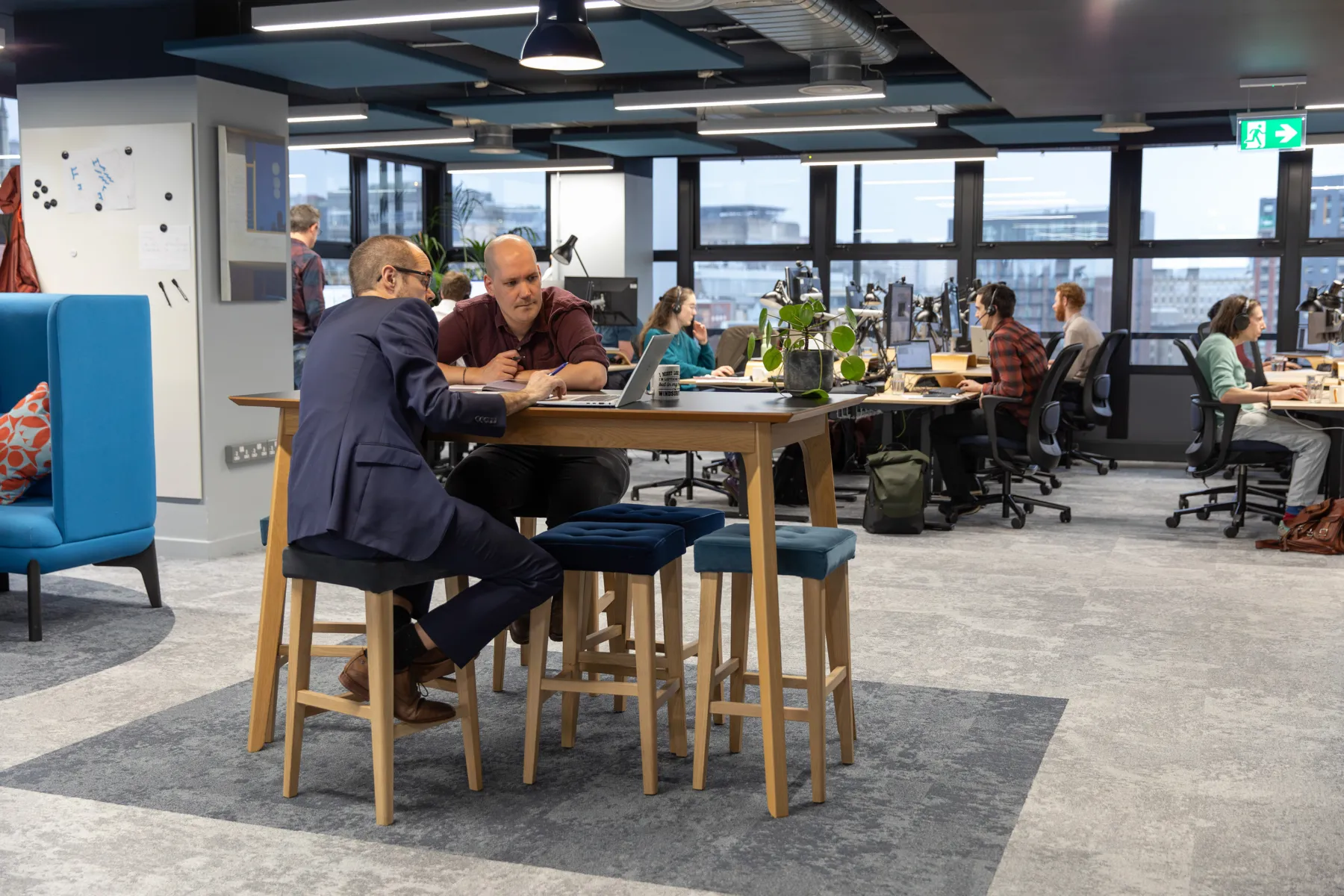 Internal view of the office, with people sitting at raised desk in the foreground, and windows in the background