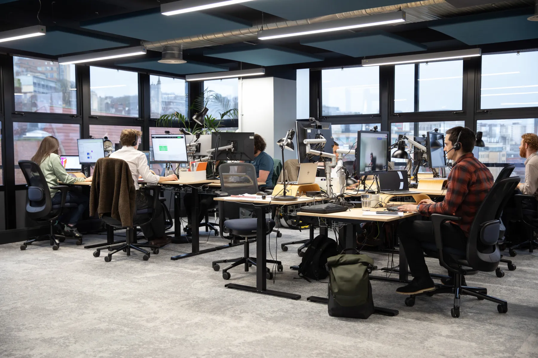 Internal view of the office, with people sitting at desks, and windows in the background