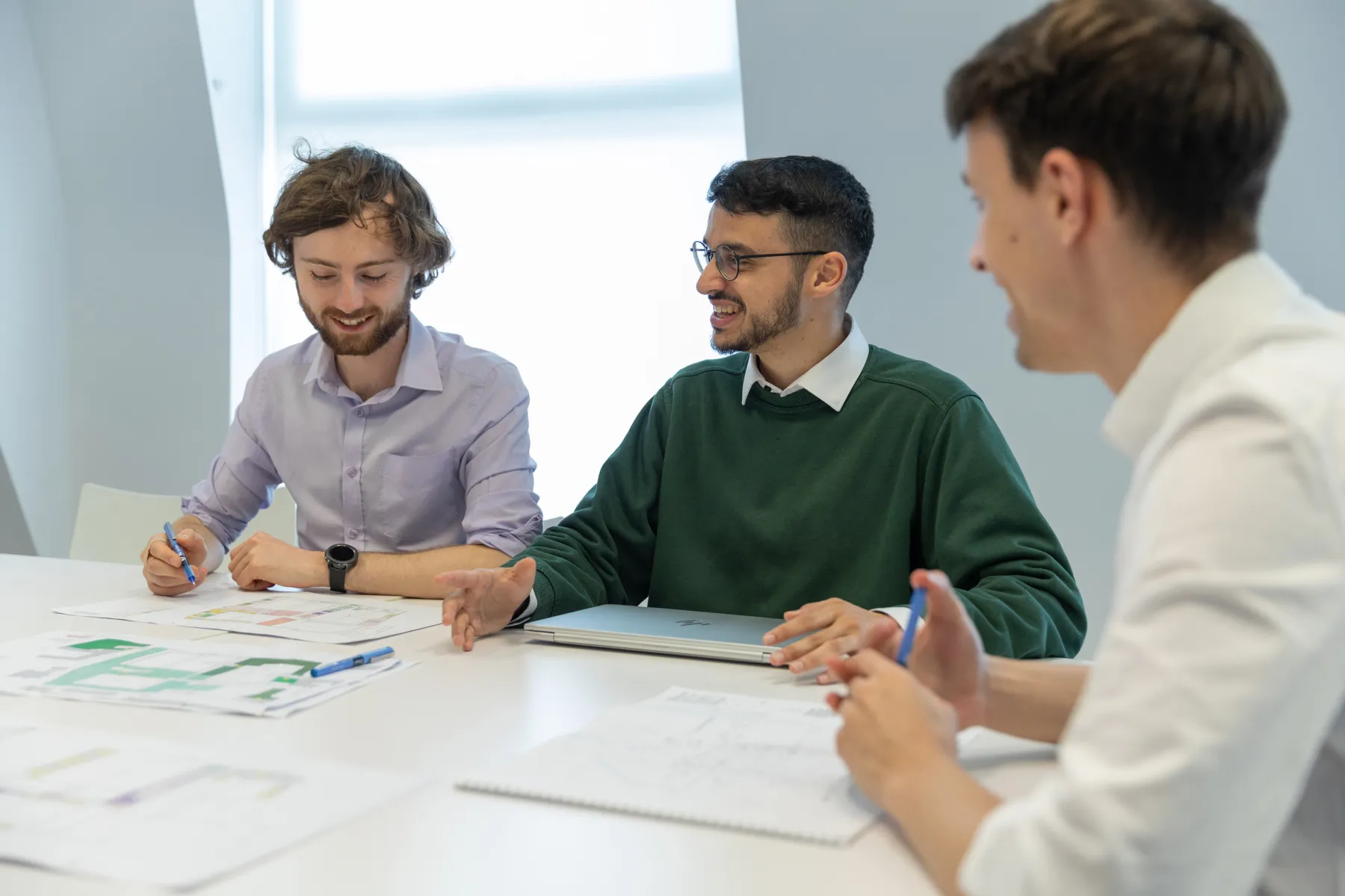 Three people looking at paper drawings of buildings