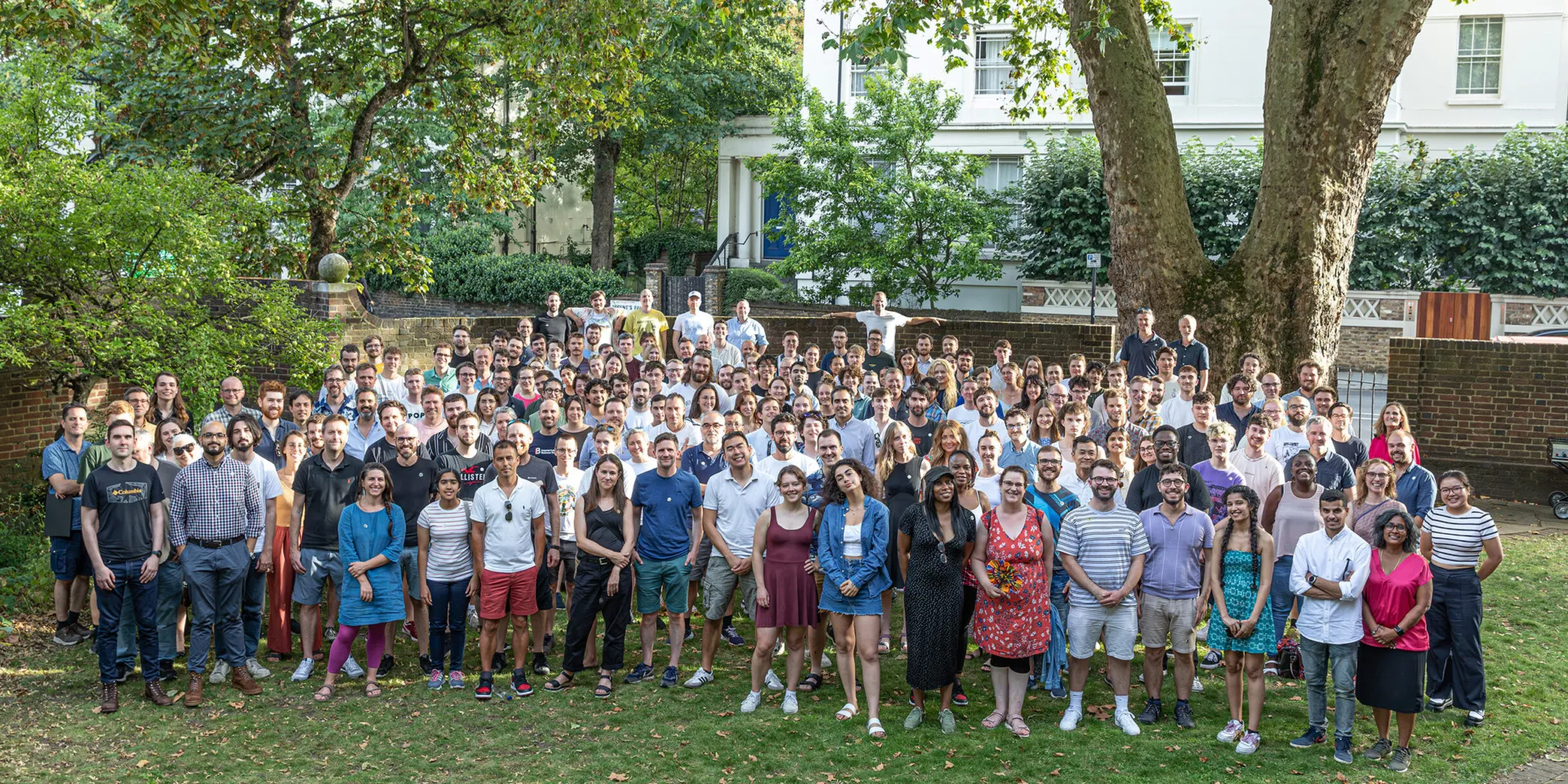 A group of more than 200 people standing in a garden smiling at the camera