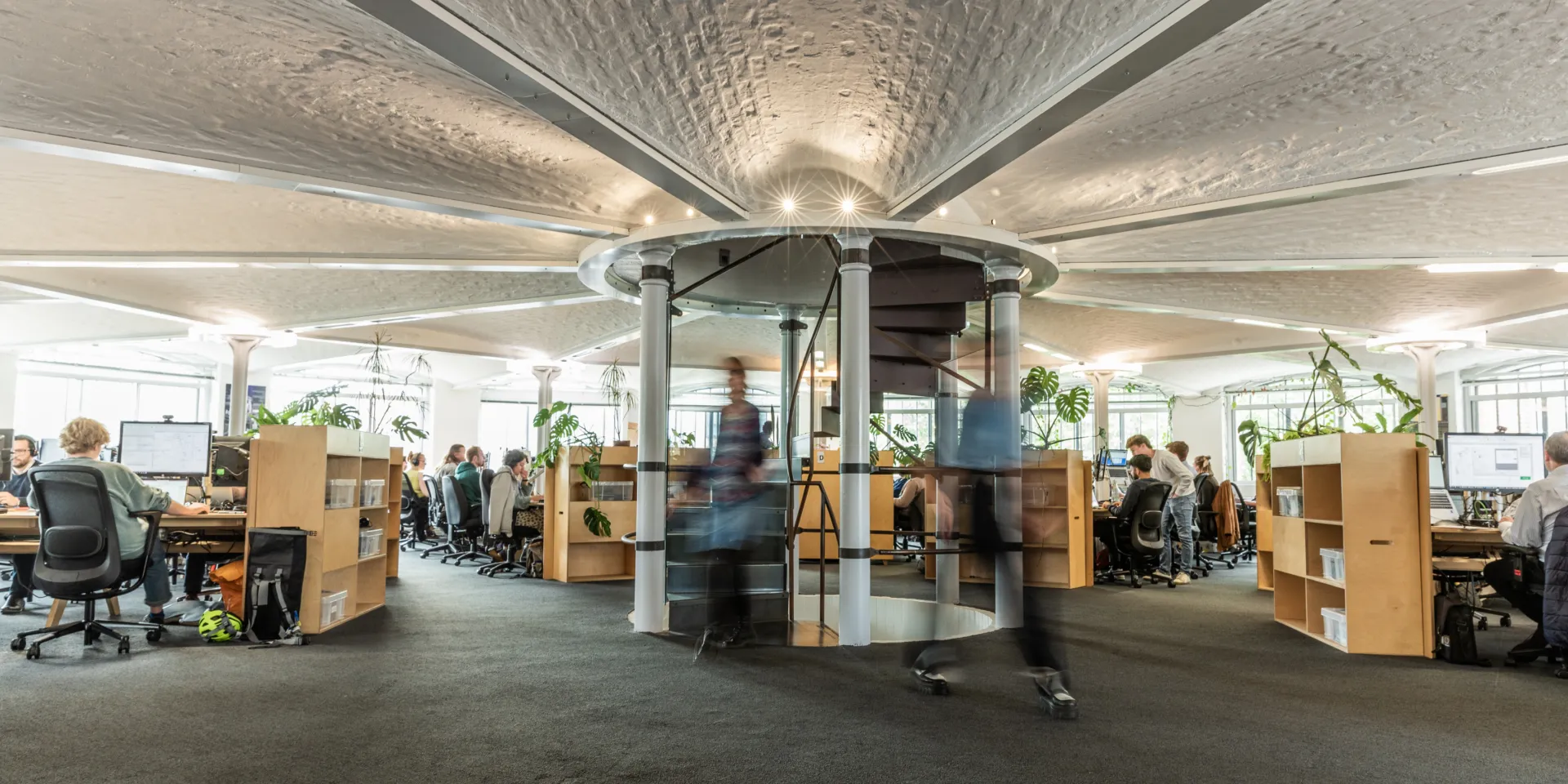 Open-plan office with central spiral staircase and exposed vaulted ceiling.