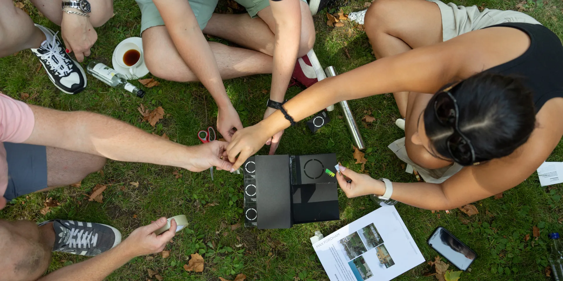 Photo from above of people's hands, making a cardboard model of a building