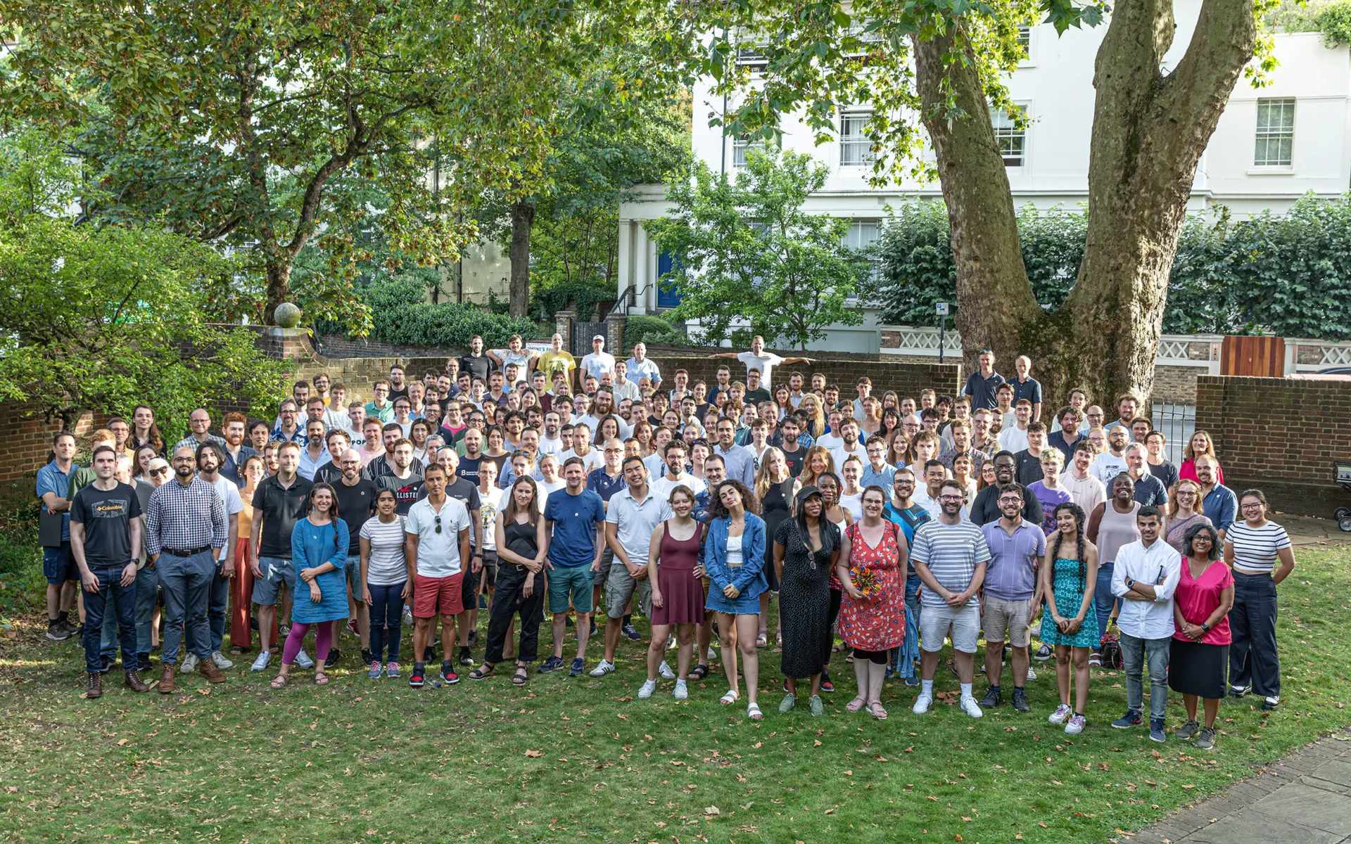 A group of more than 200 people standing in a garden smiling at the camera