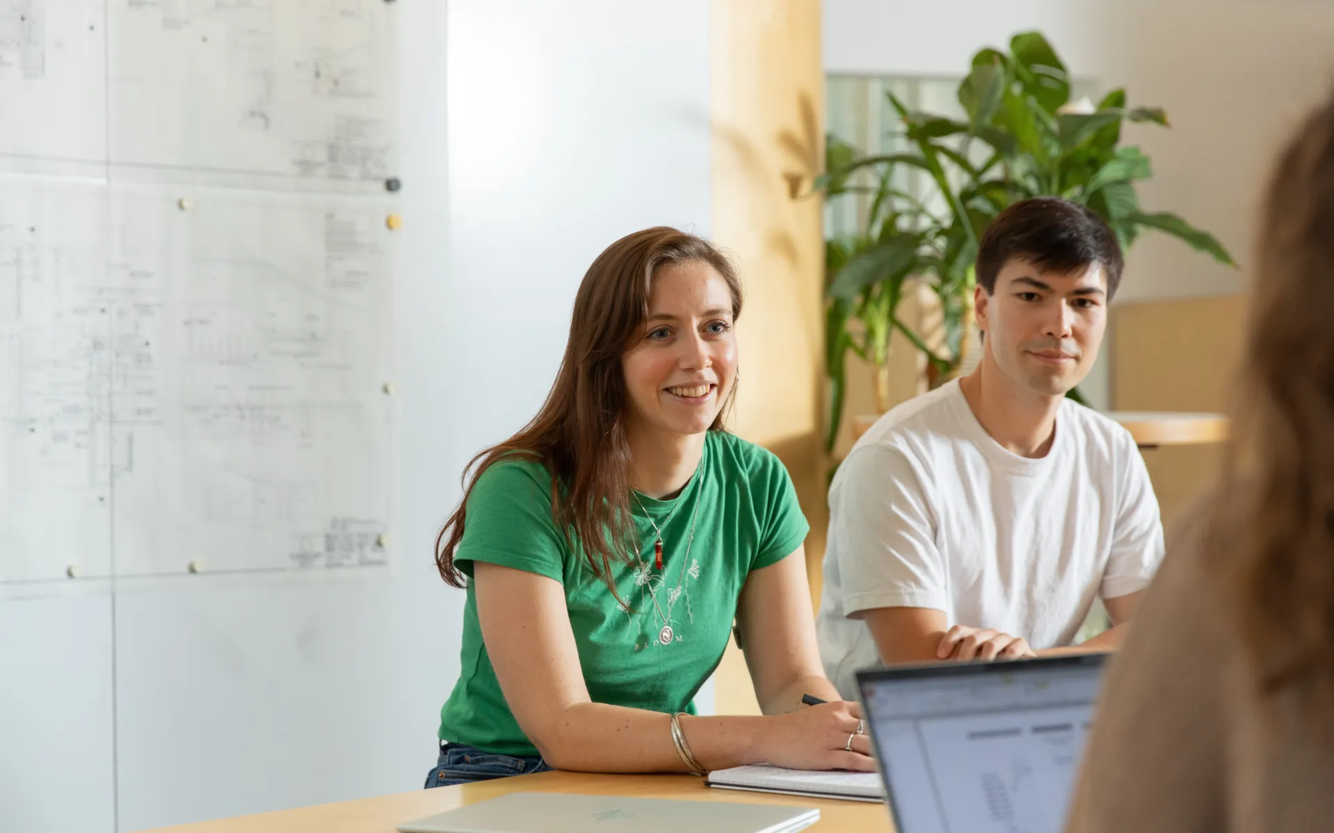 Three people sitting and chatting in a bright office with laptops and documents on the table