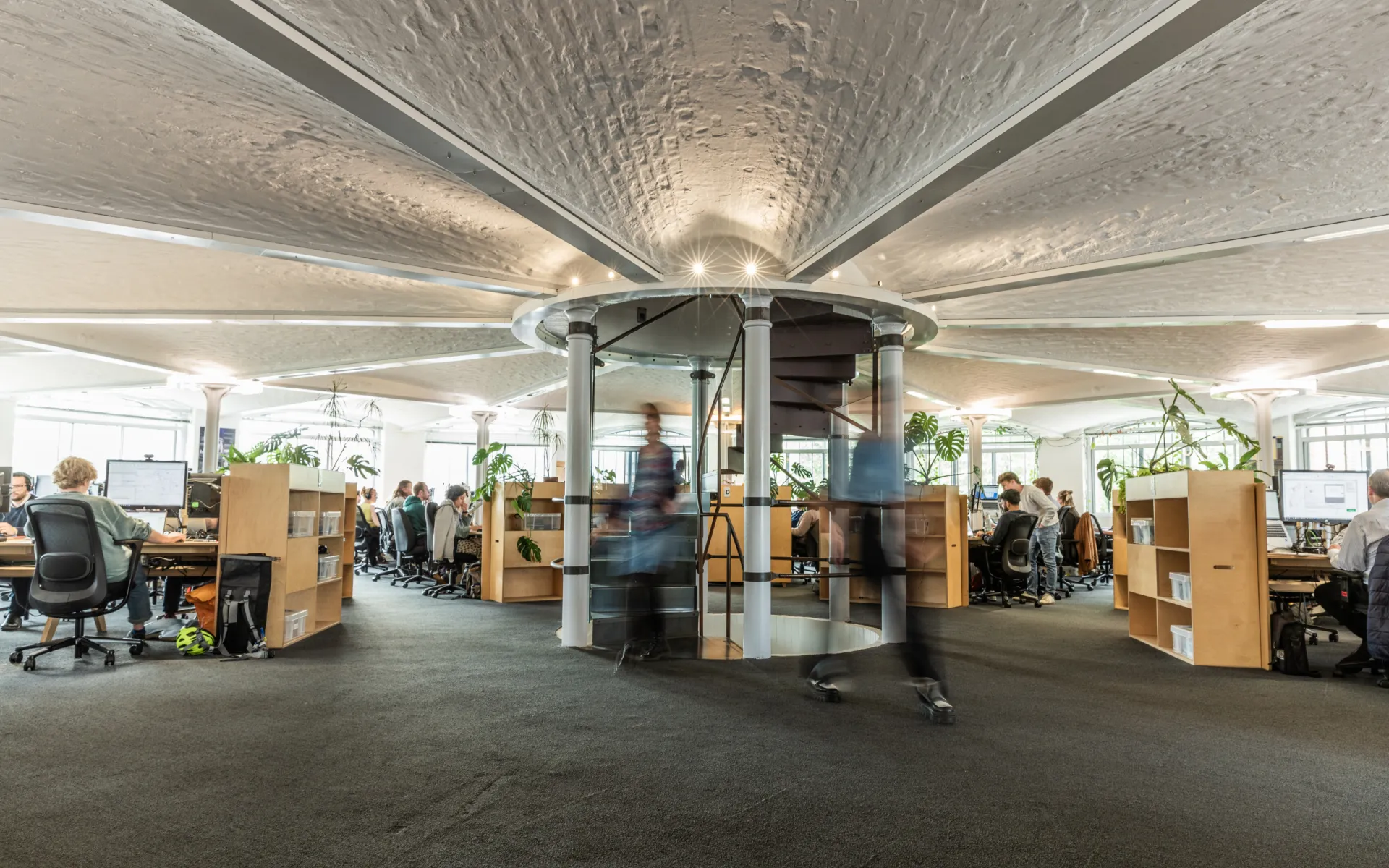 Open-plan office with central spiral staircase and exposed vaulted ceiling.