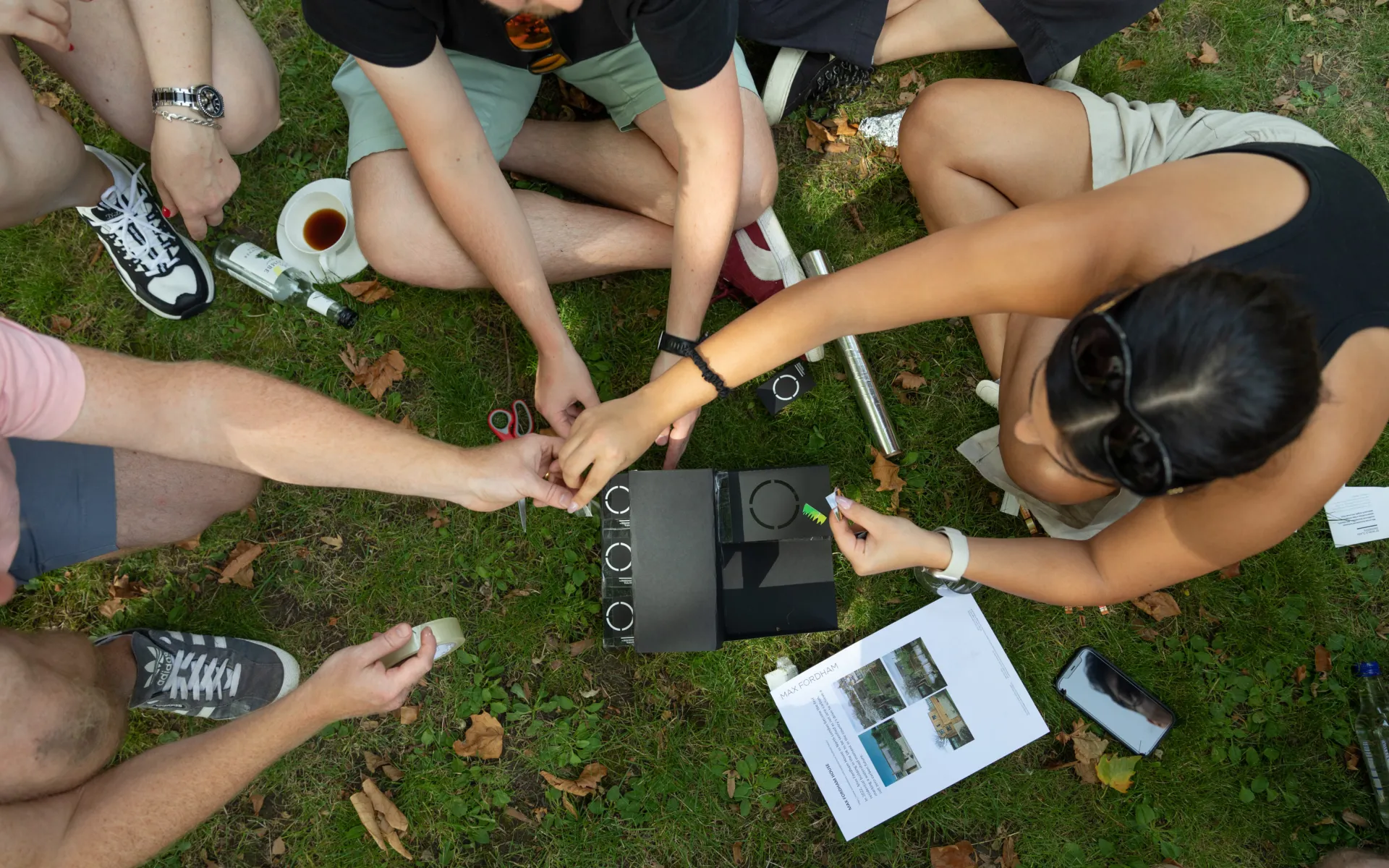 Photo from above of people's hands, making a cardboard model of a building