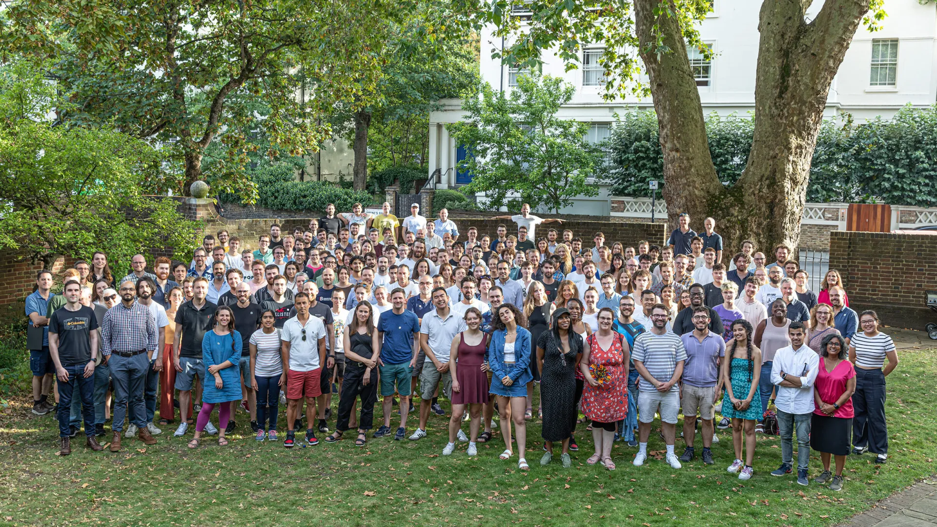 A group of more than 200 people standing in a garden smiling at the camera