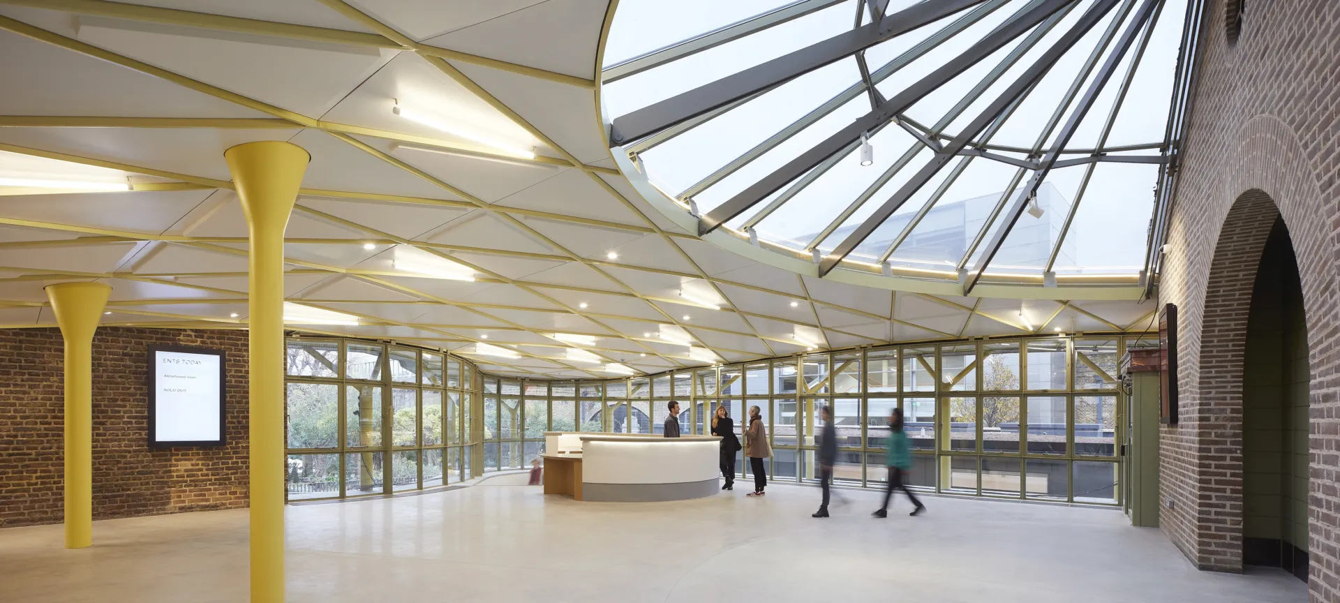 Five people stand beside the reception desk in the large glazed and red brick foyer of Museum of the Home.