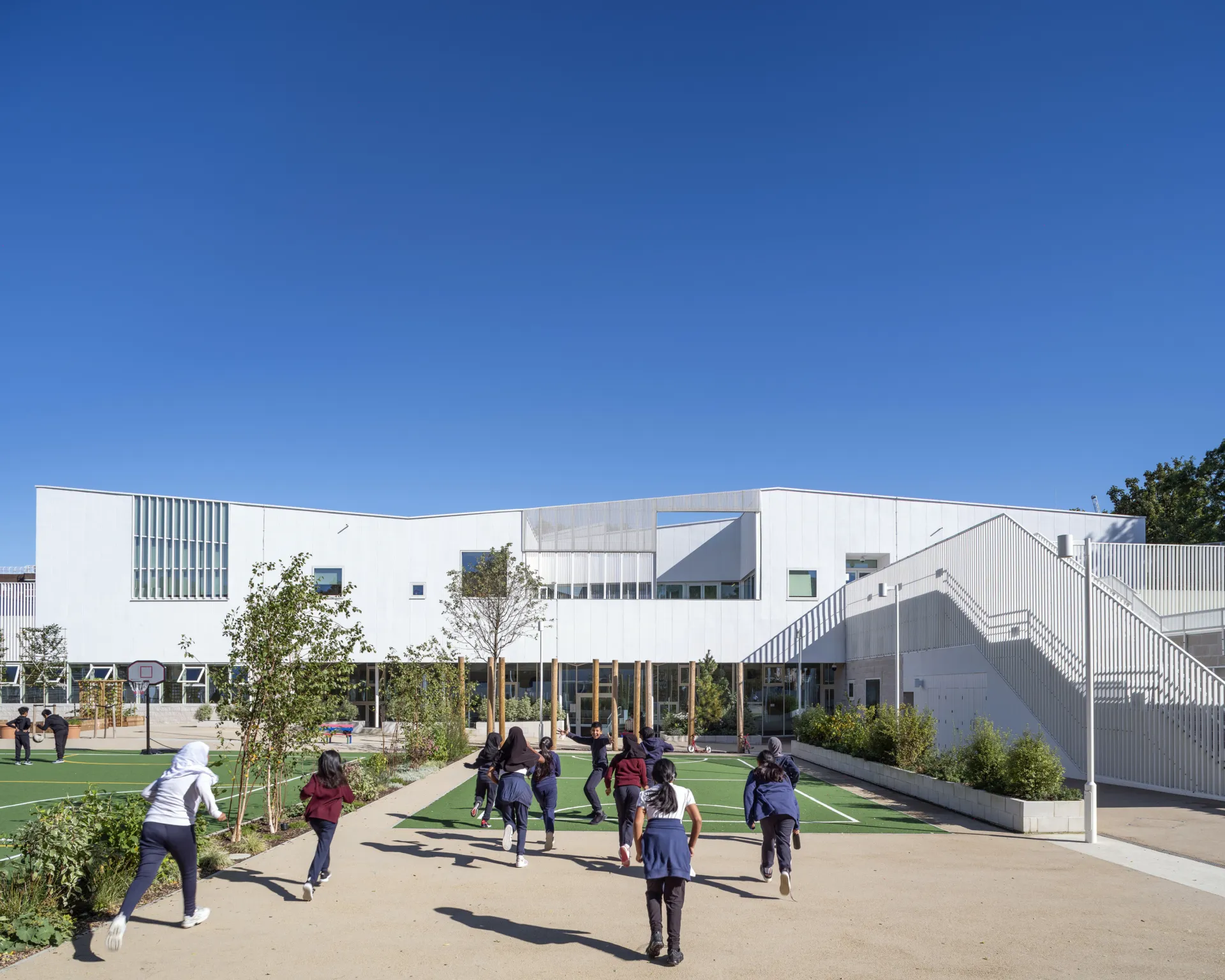 Teenage pupils run owards the entrance of Edith Neville School, a large white modern building.