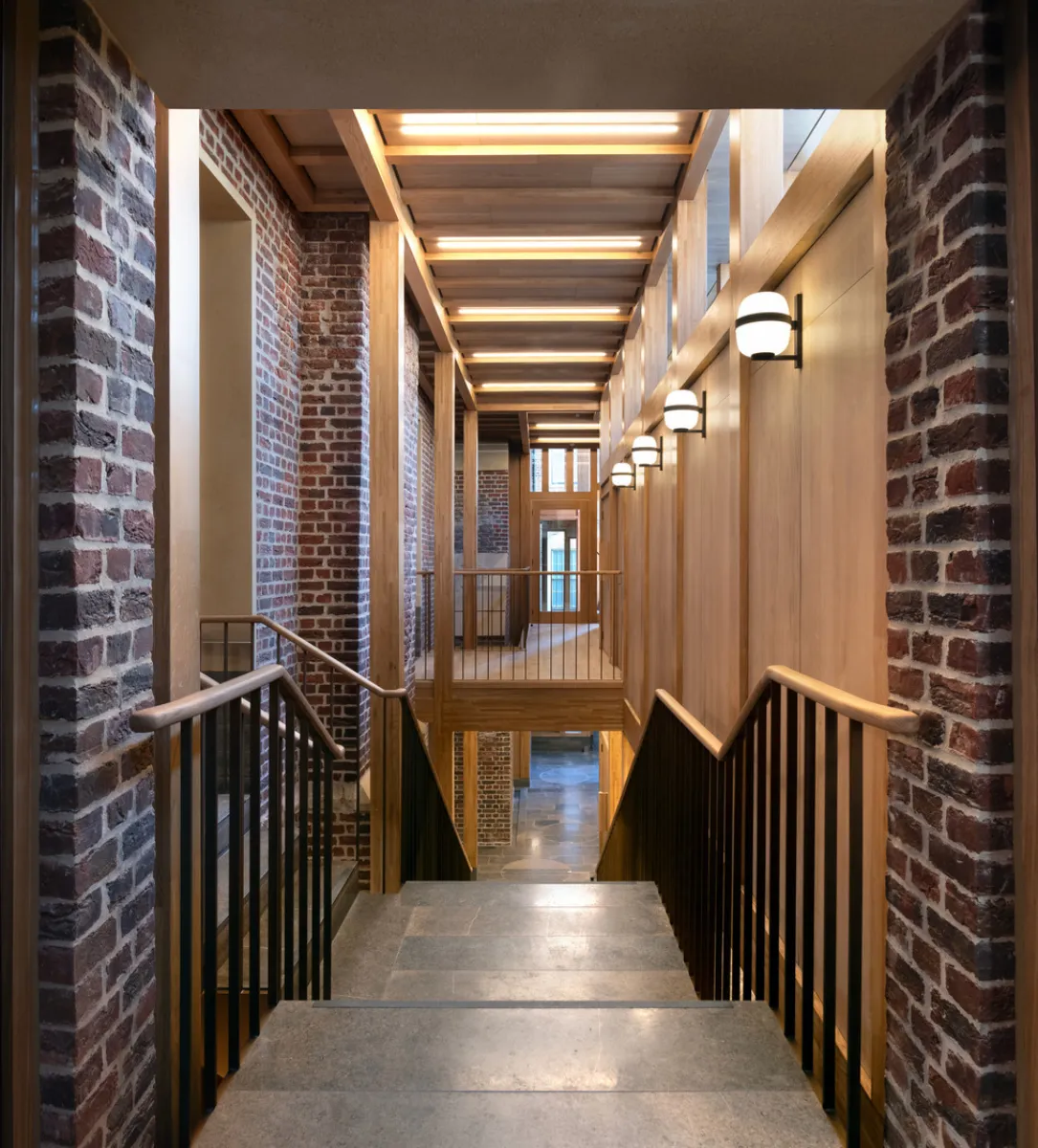 corridor with steps leading down with brick walls and handrails