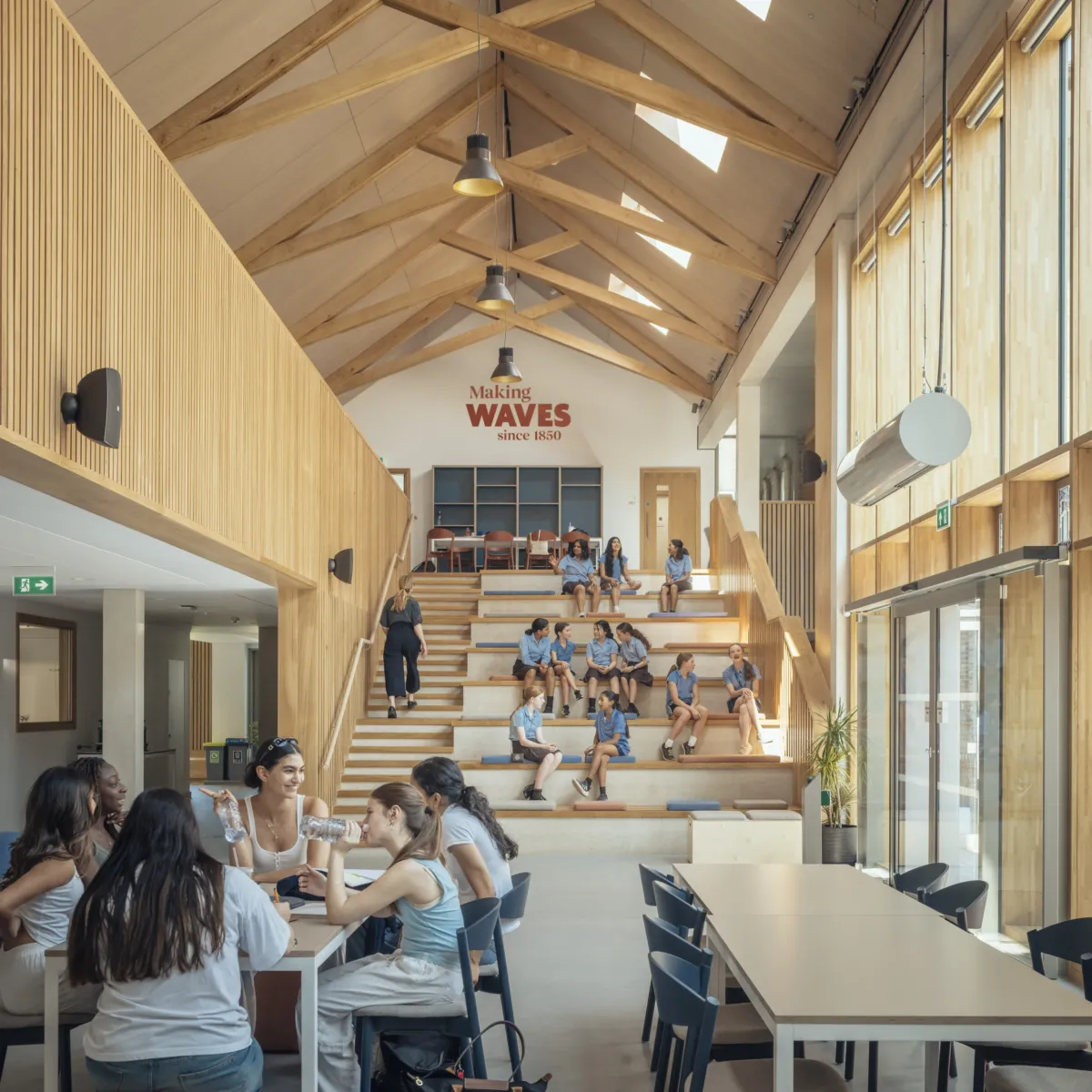 Student gathered on large staircase and sitting at tables in light-filled room