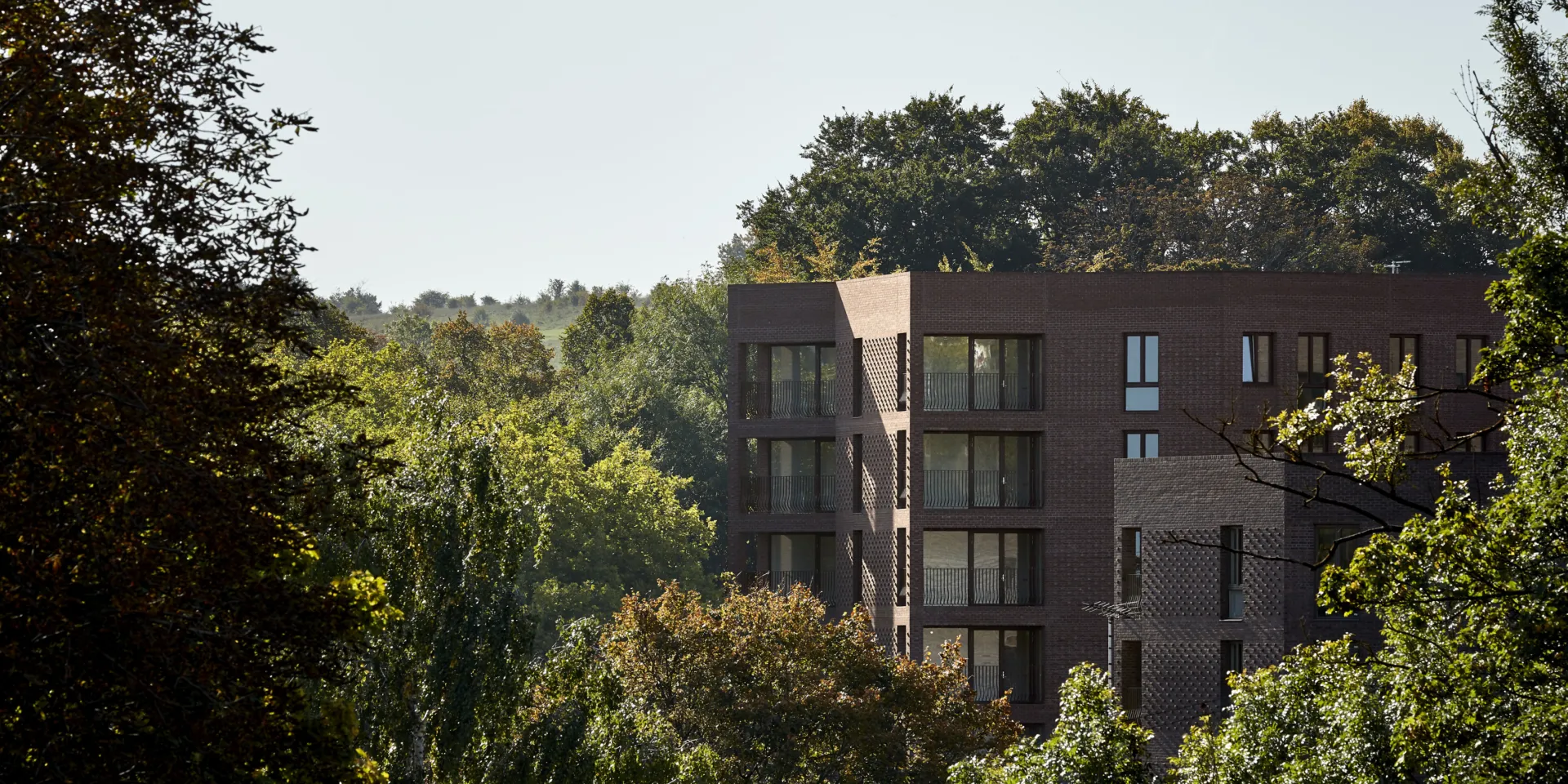 Brick-clad apartment building nestled among mature trees and greenery.