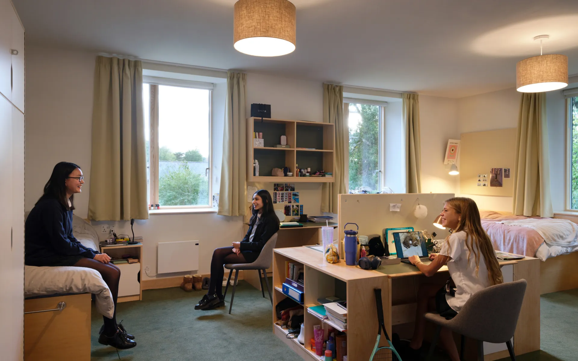 Students sat chatting in one of the new shared-bedrooms, in daylight but with the ceiling lights switched on.