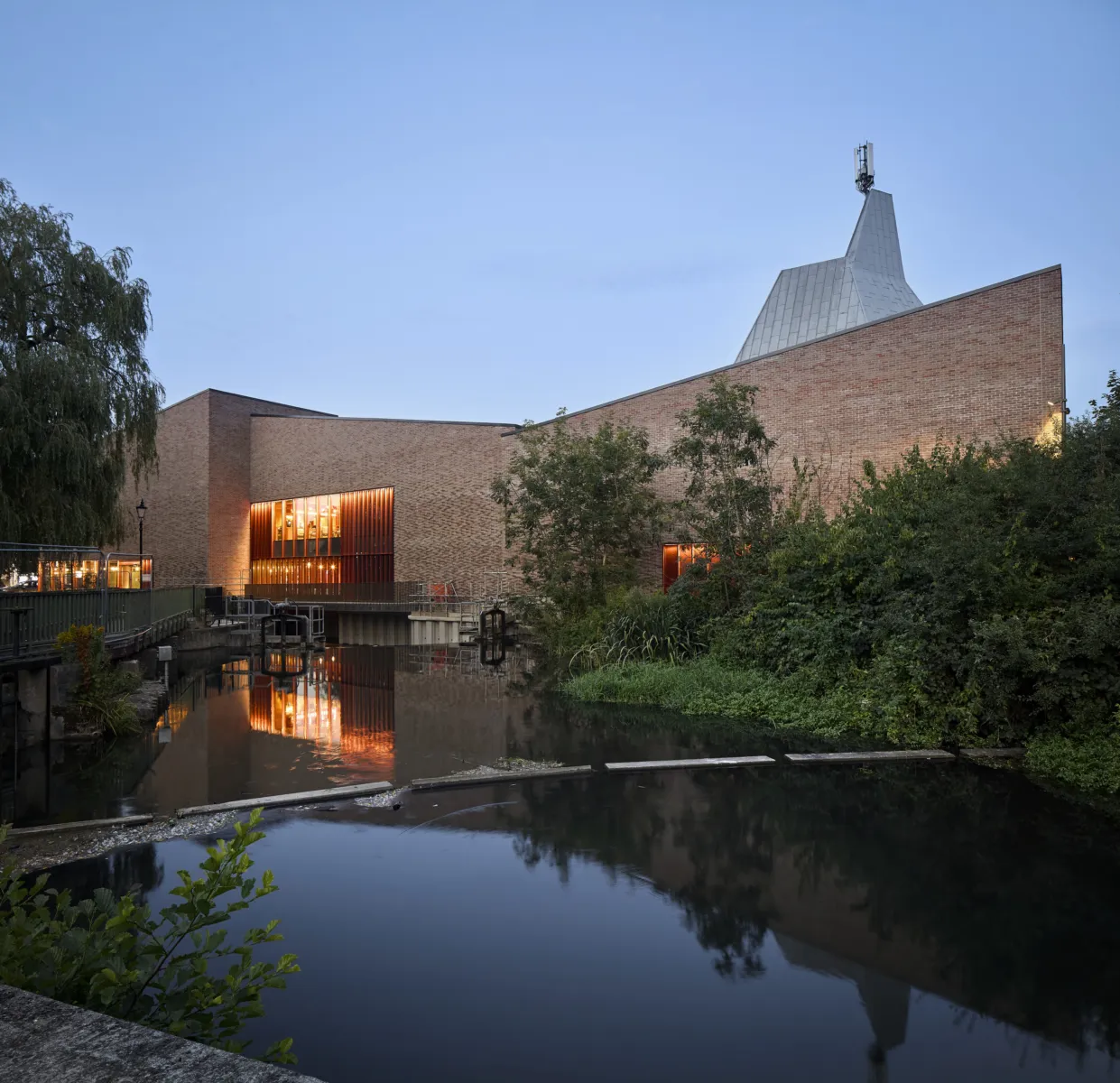 red brick building at dusk with warm lighting and with water in front