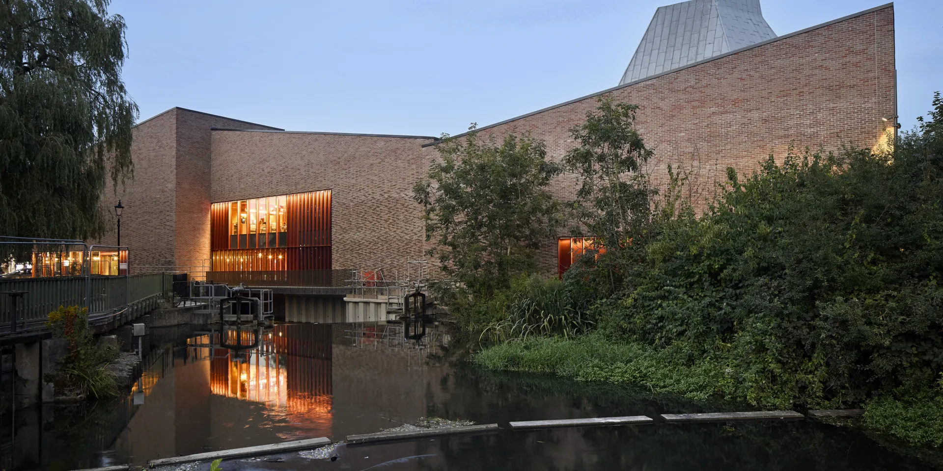 red brick building at dusk with warm lighting and with water in front