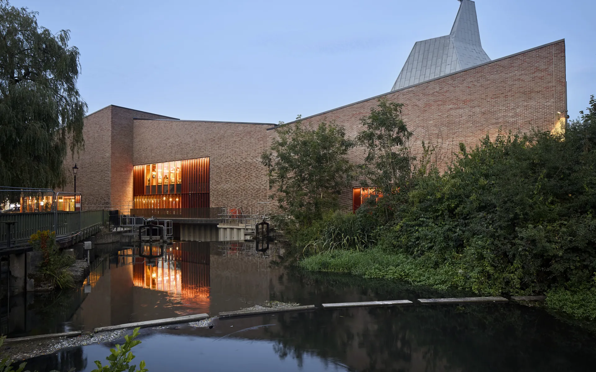red brick building at dusk with warm lighting and with water in front