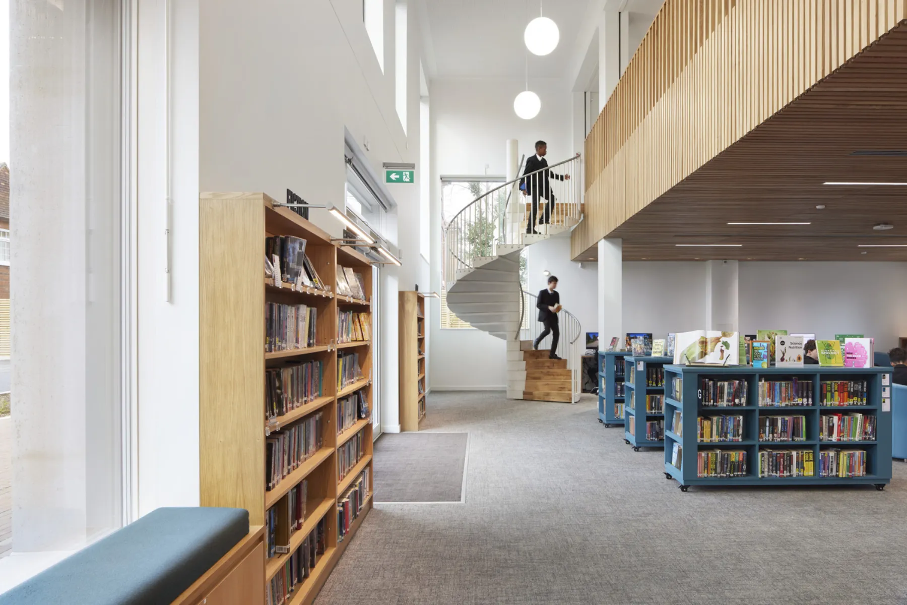Wooden bookcases in a white light-filled library. Spiral staircase