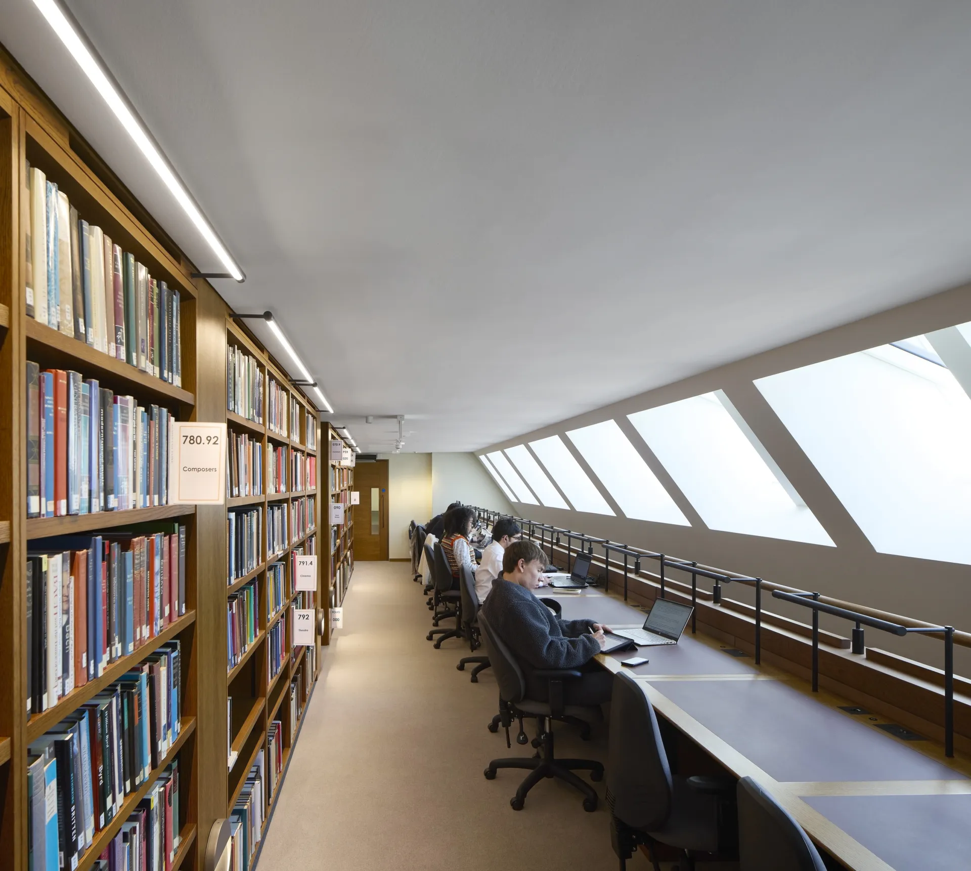 People sitting at study stations with books behind them and skylights.