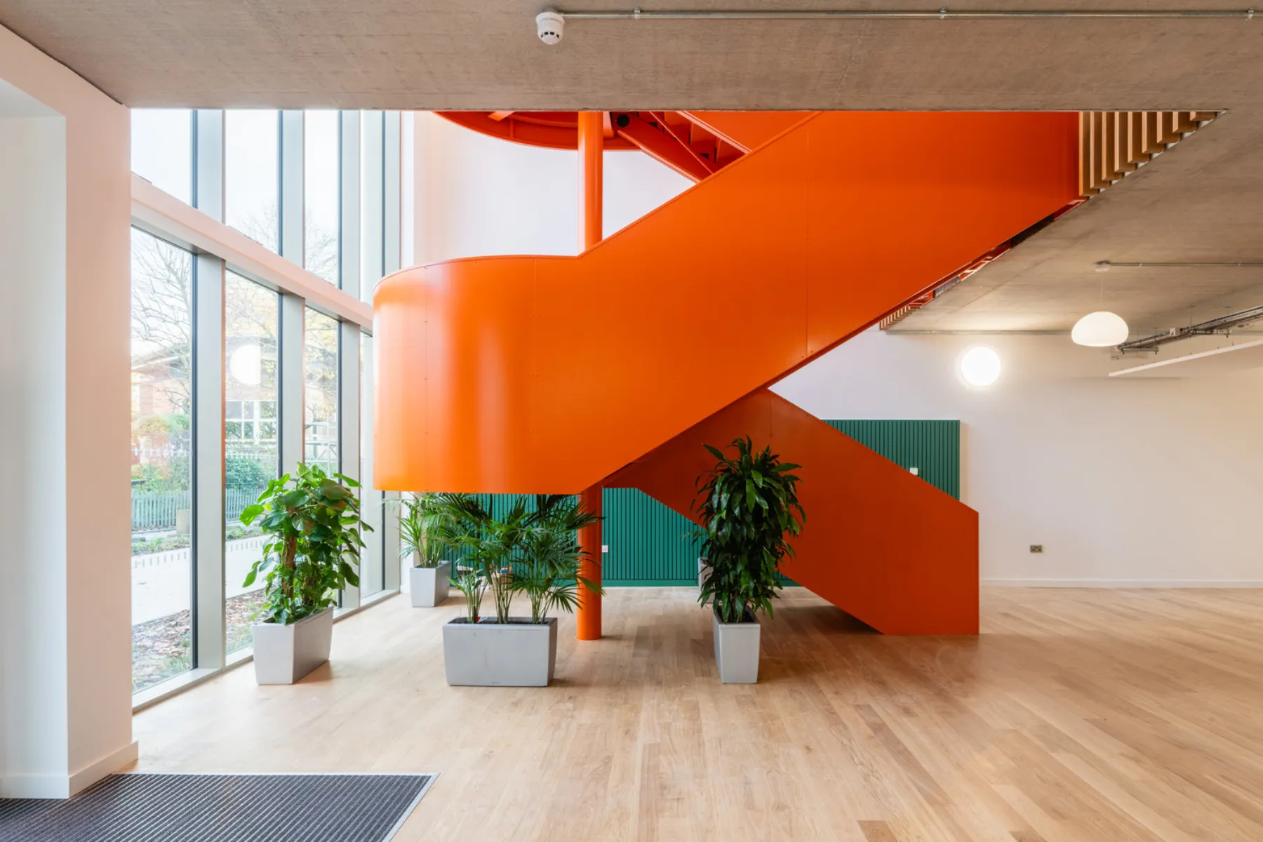 Light-filled interior featuring a striking orange staircase, timber flooring and indoor planting.