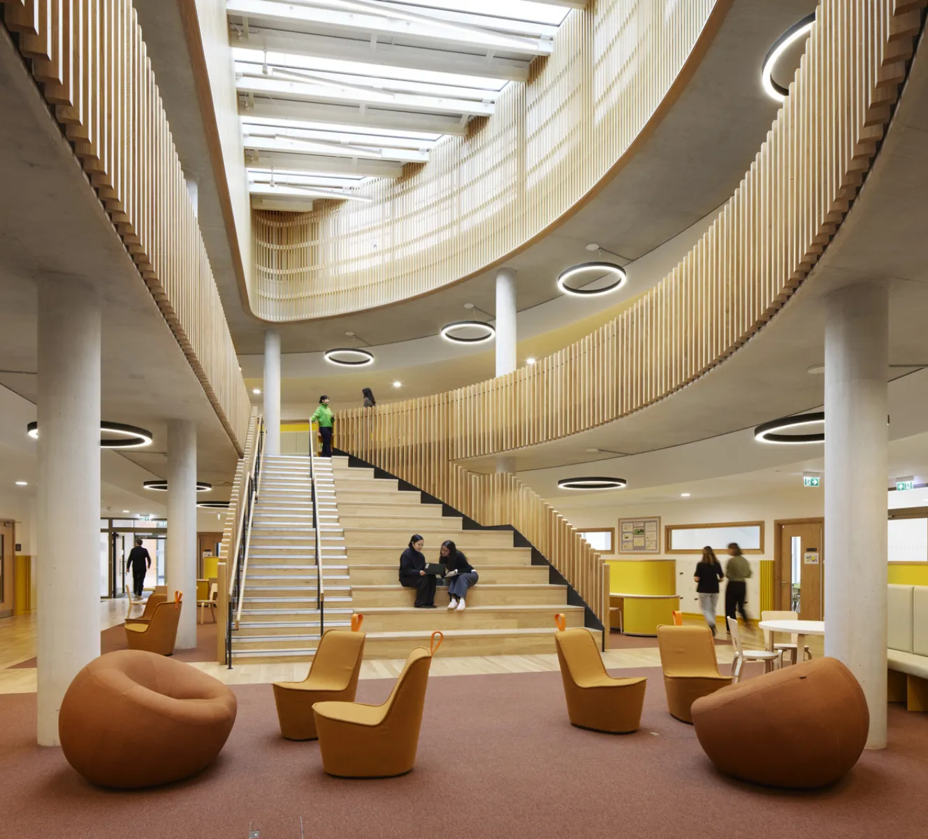 Multi-storey atrium with broad timber steps used as informal seating, surrounded by study and social spaces.