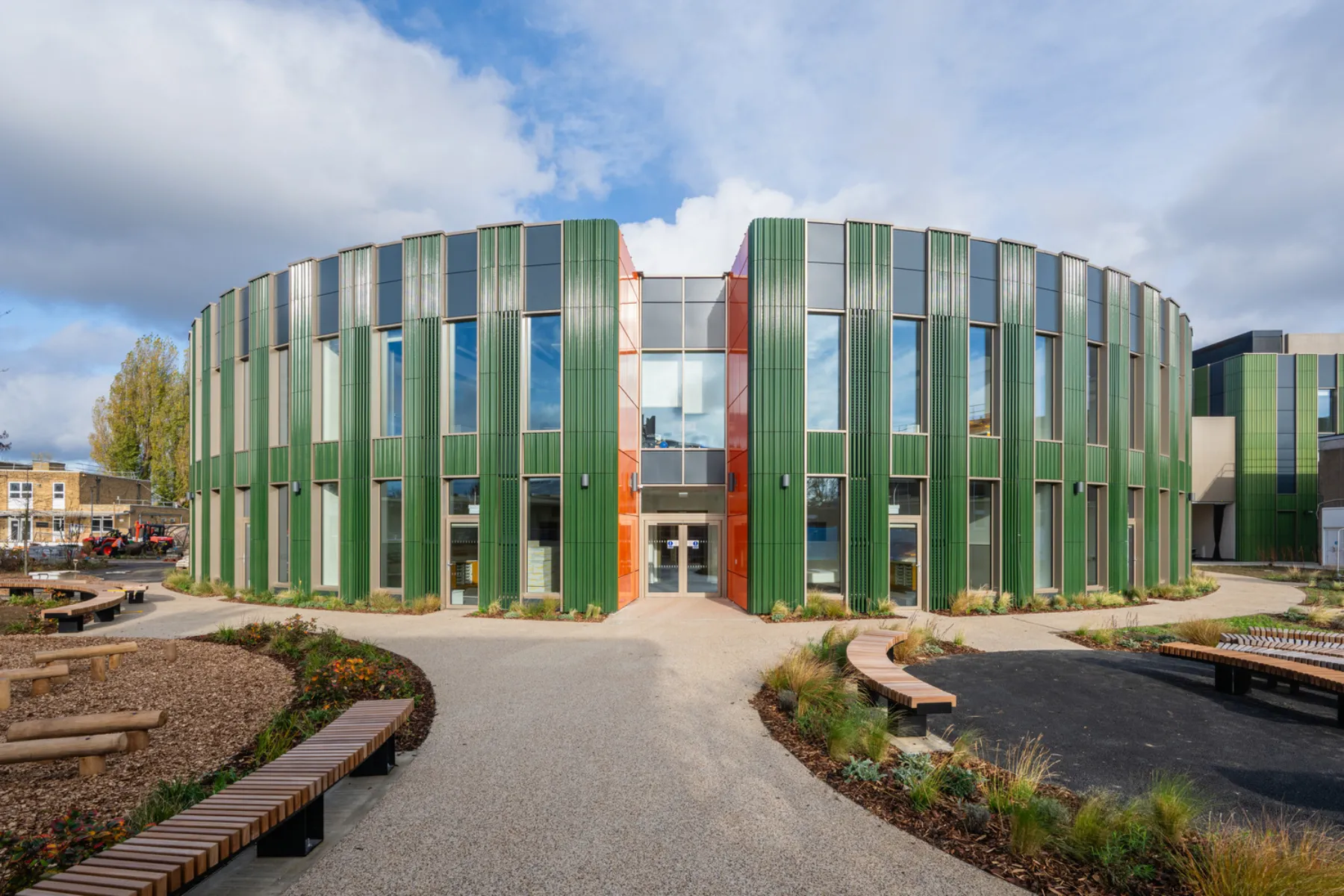 Curved school building with green vertical cladding, large windows and landscaped outdoor learning spaces.