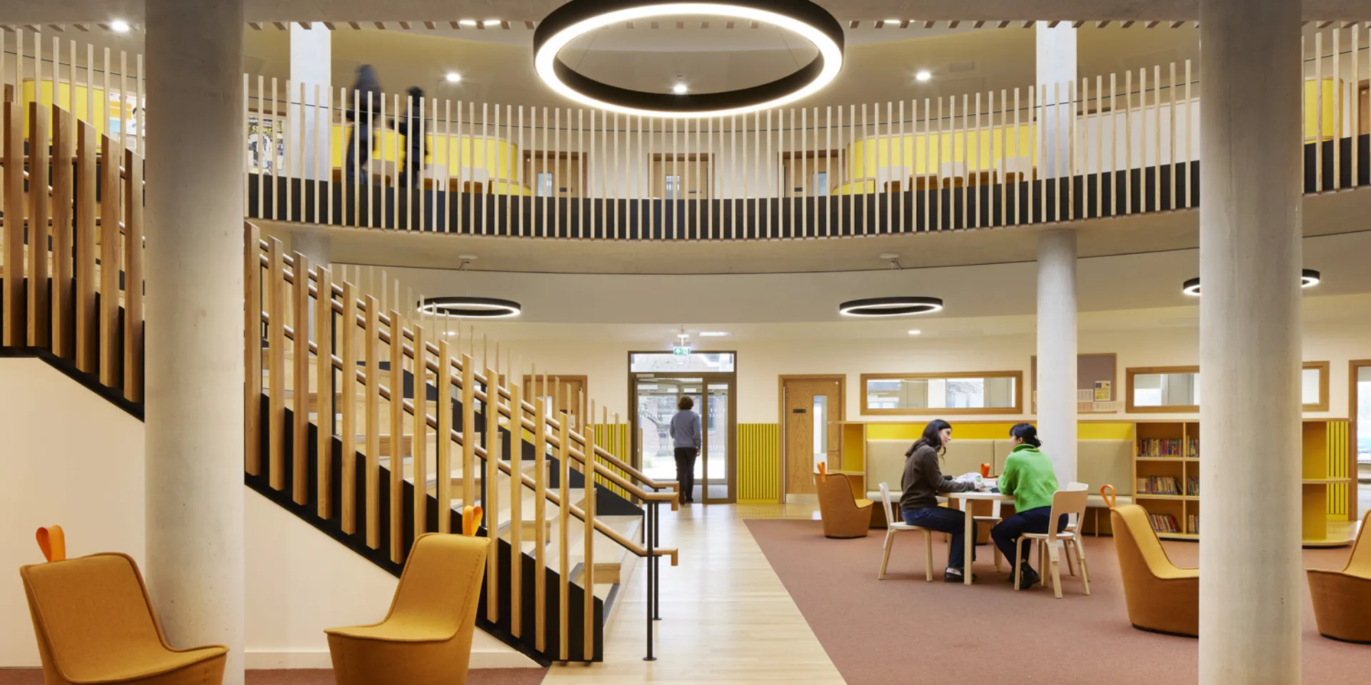 Open central atrium with wide timber staircase, circular balconies and seating areas, with people using the space.