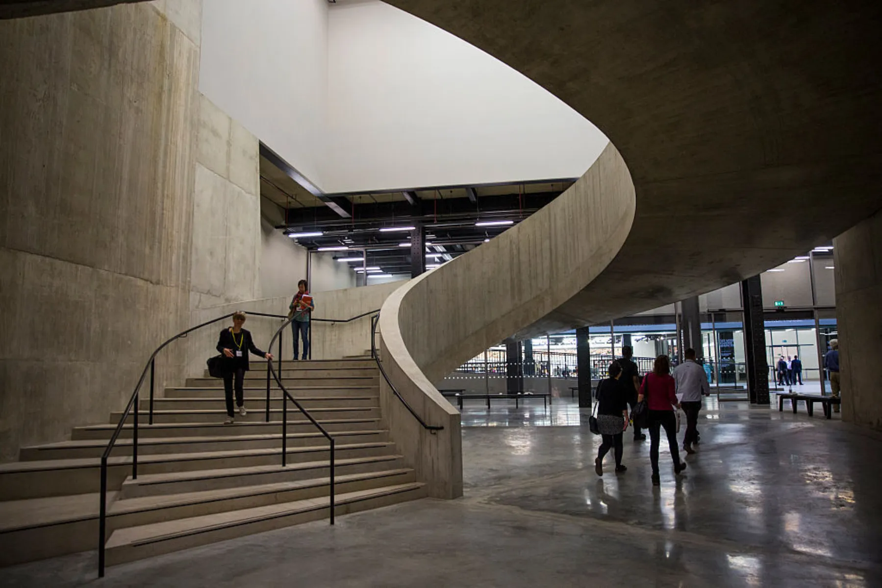 An interior of a building, with a large curved concrete staircase, lit diffusely from above