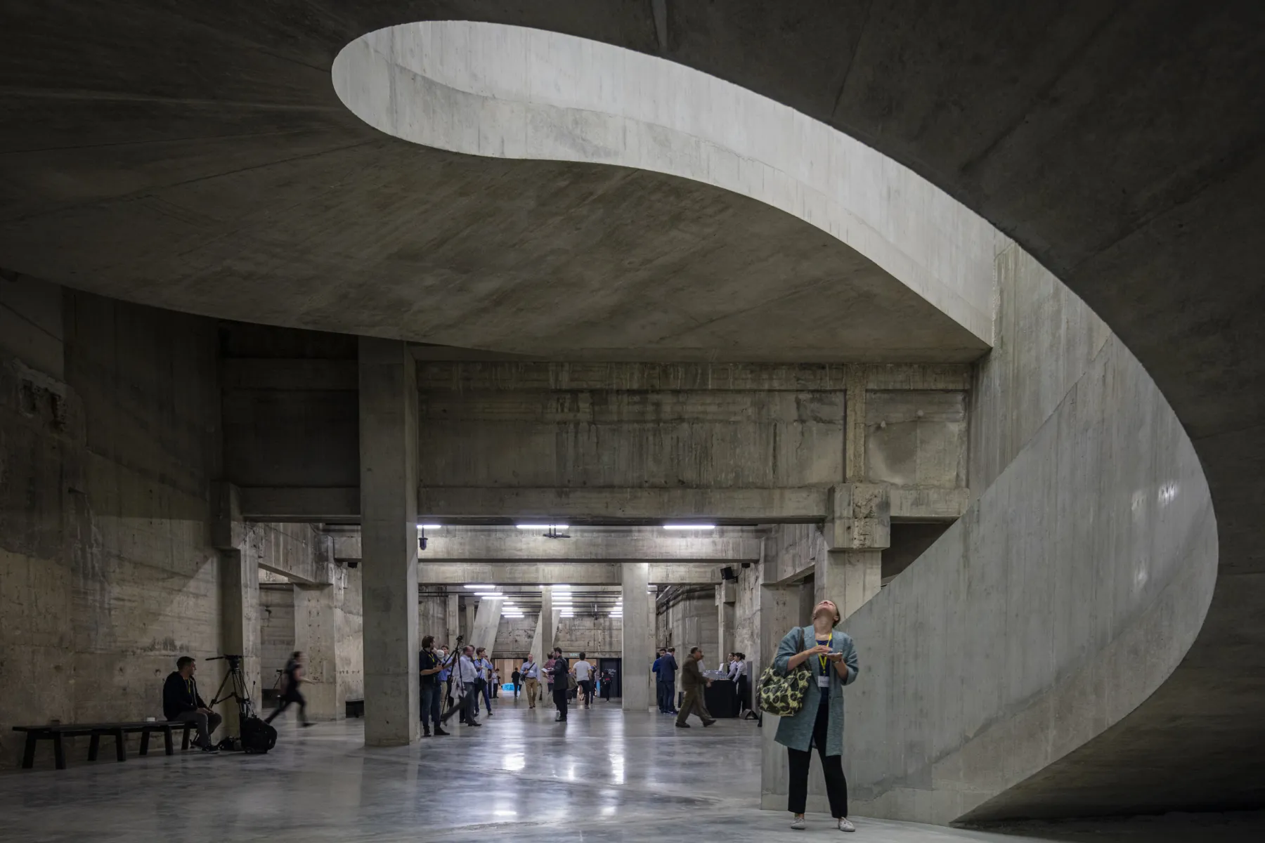 A concrete interior space, with light coming from a large curved concrete stairwell