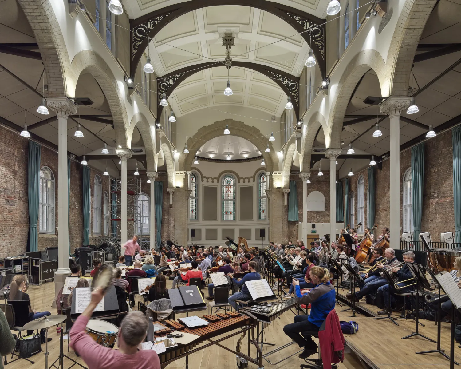 An orchestra rehearsing in a venue with a high arched celling
