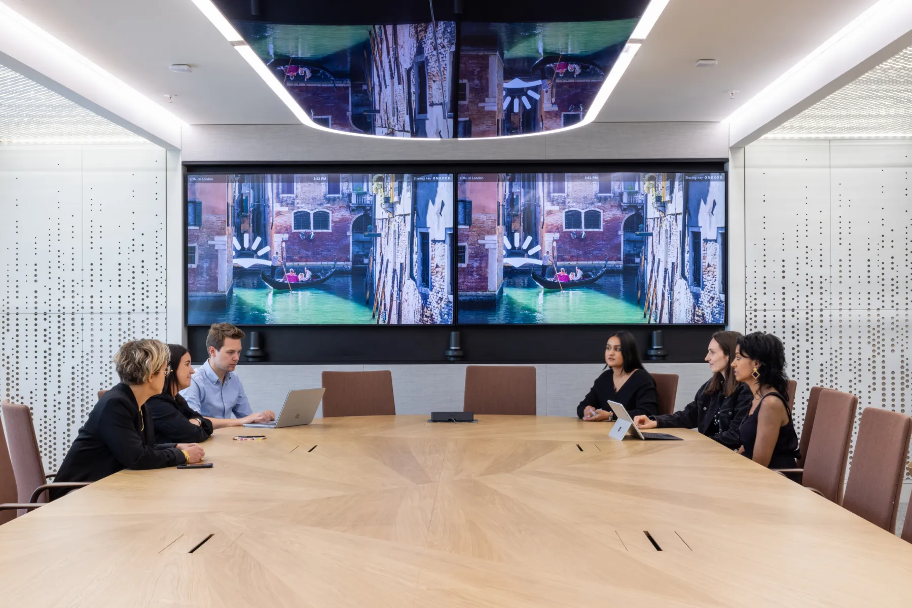 A conference room with people sitting around a large screen for a meeting