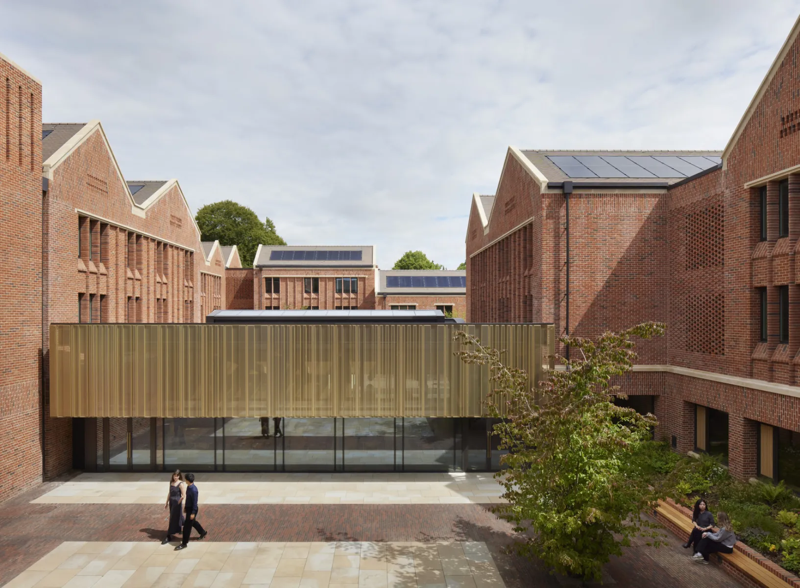 Central courtyard framed by brick boarding houses, with a glazed and metal-clad shared building linking the accommodation blocks.