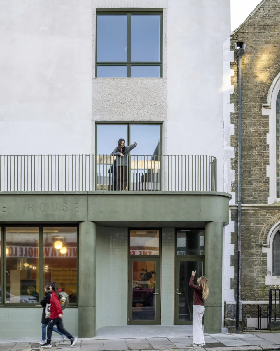 Person standing on a balcony above the entrance of a modern building.