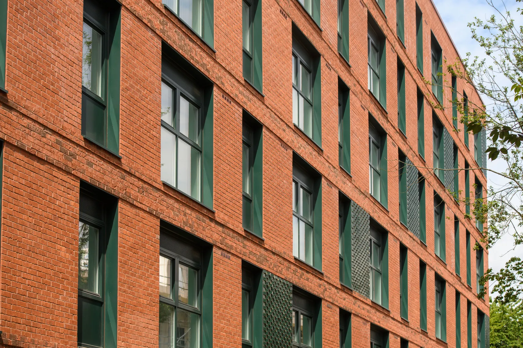 Close-up of a curved red-brick residential façade with deep-set windows and dark green metal detailing.